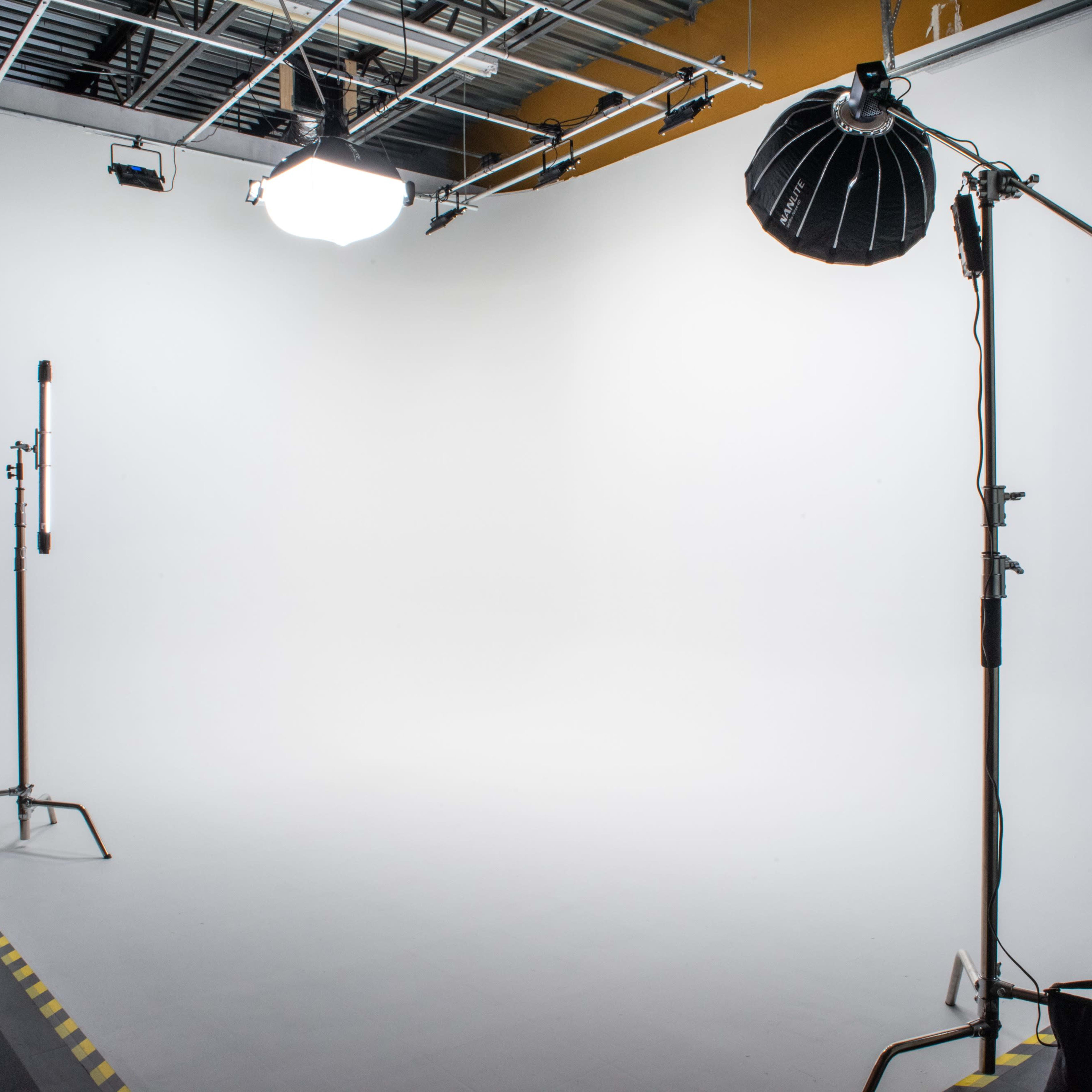 A photography studio with a white backdrop and lighting equipment positioned on stands.