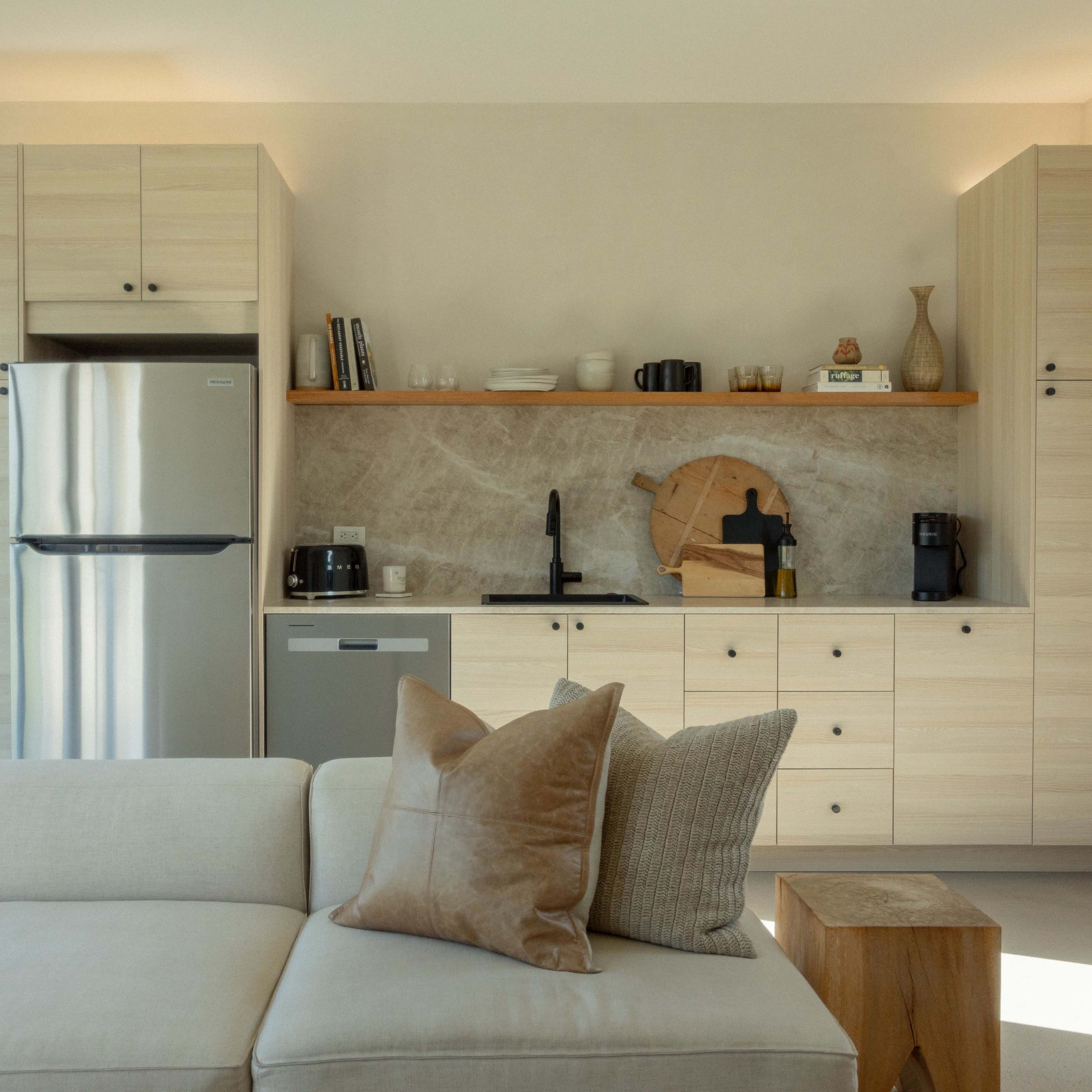A modern kitchen with light wood cabinetry, stainless steel appliances, and a neutral-colored countertop.