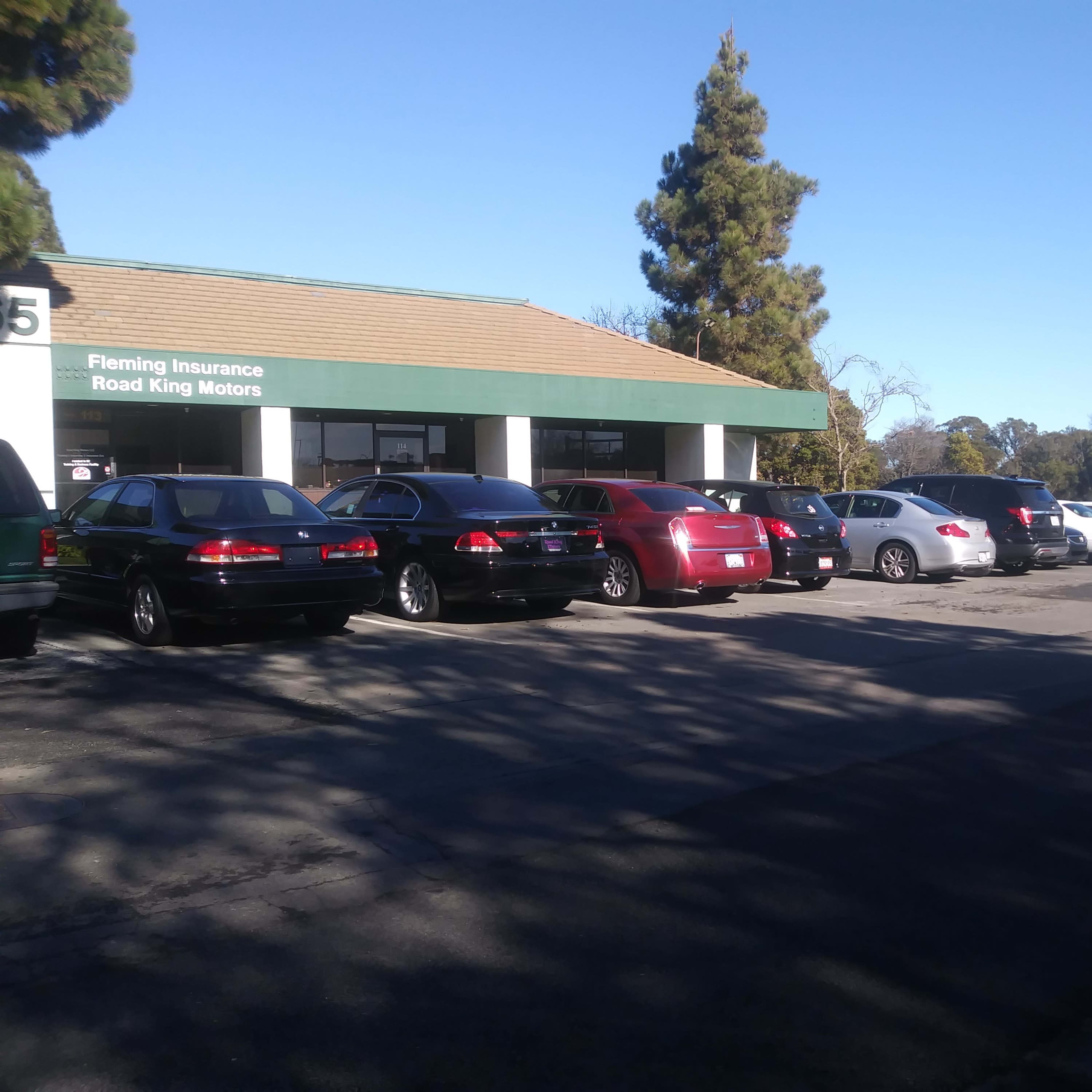 A row of parked cars is lined up in front of a building with a sign for Fleming Insurance and Road King Motors.