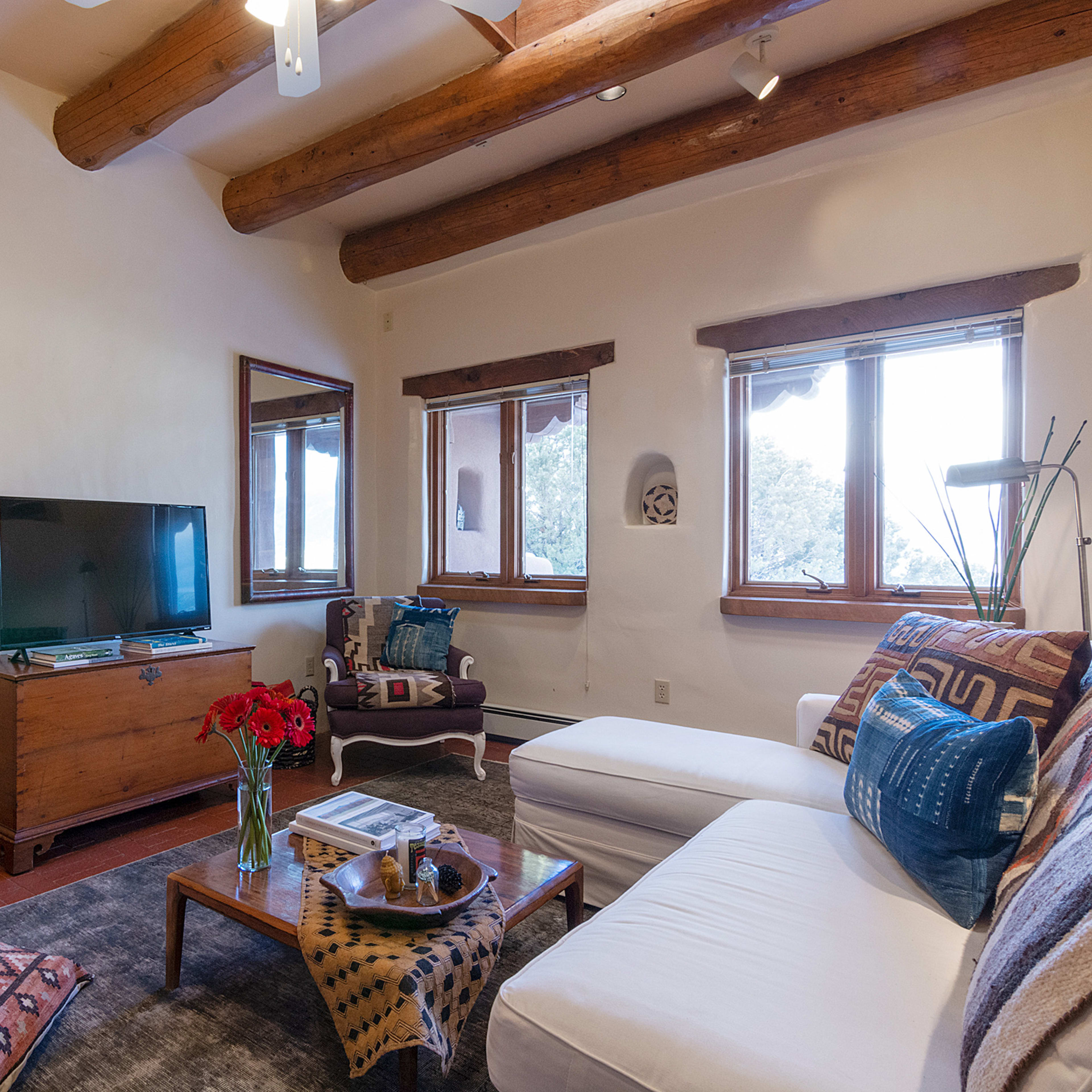 The room features a white sofa, a wooden coffee table with a decorative bowl, a television, and a fireplace, surrounded by windows that provide natural light.