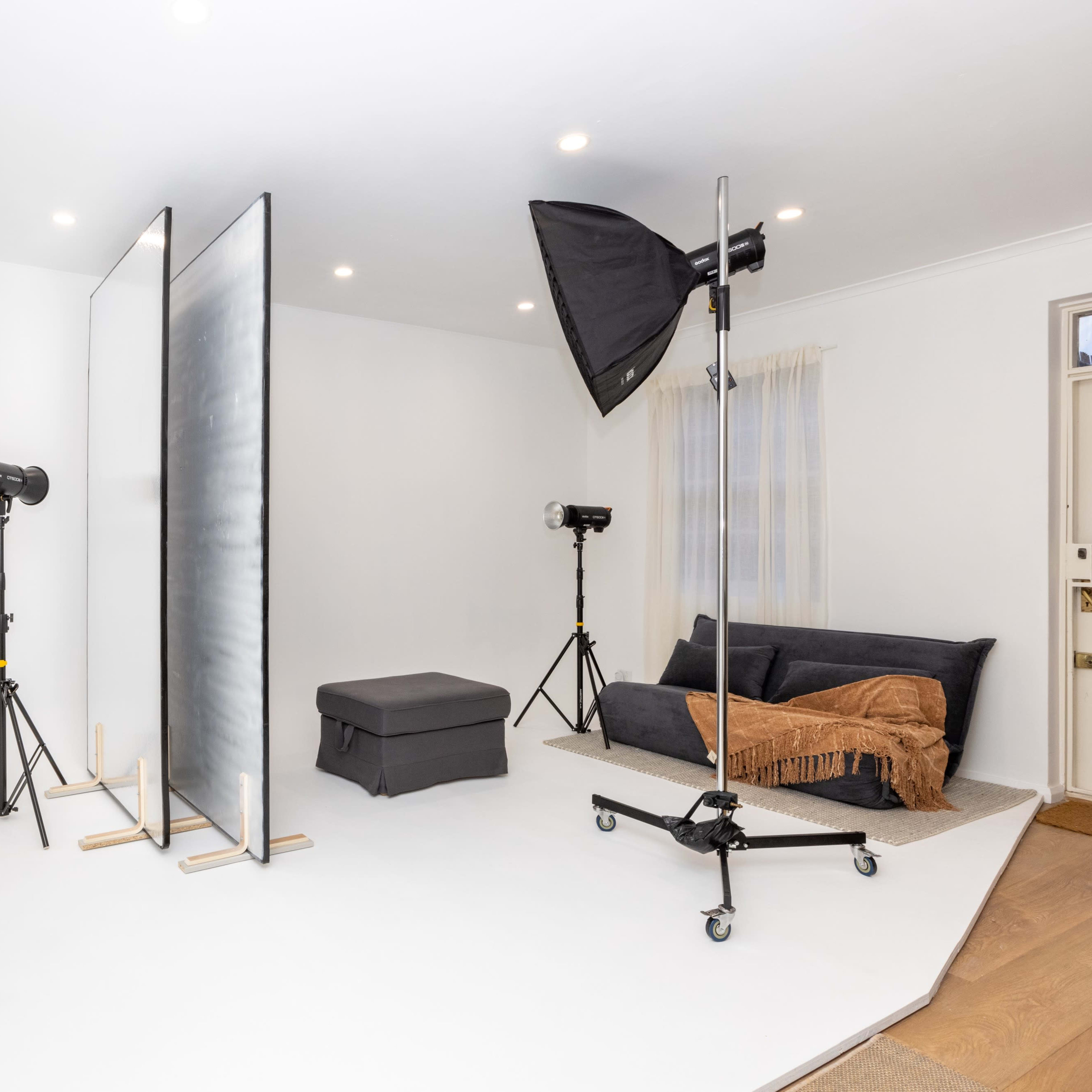 A minimalist photography studio with a gray couch, two softbox lights on stands, and a backdrop setup.