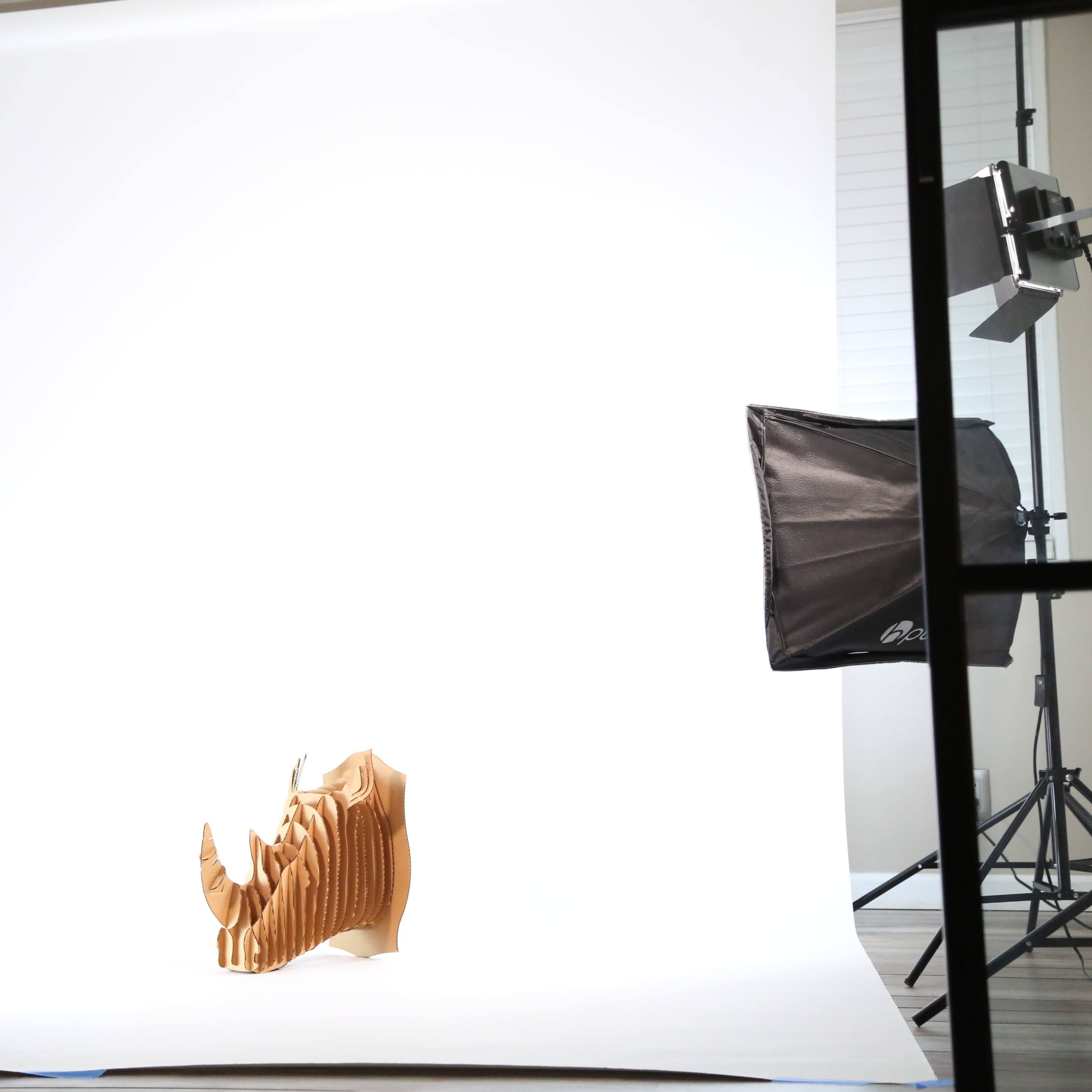 A wooden sculpture of a rhinoceros positioned against a bright white backdrop in a well-lit studio setting.