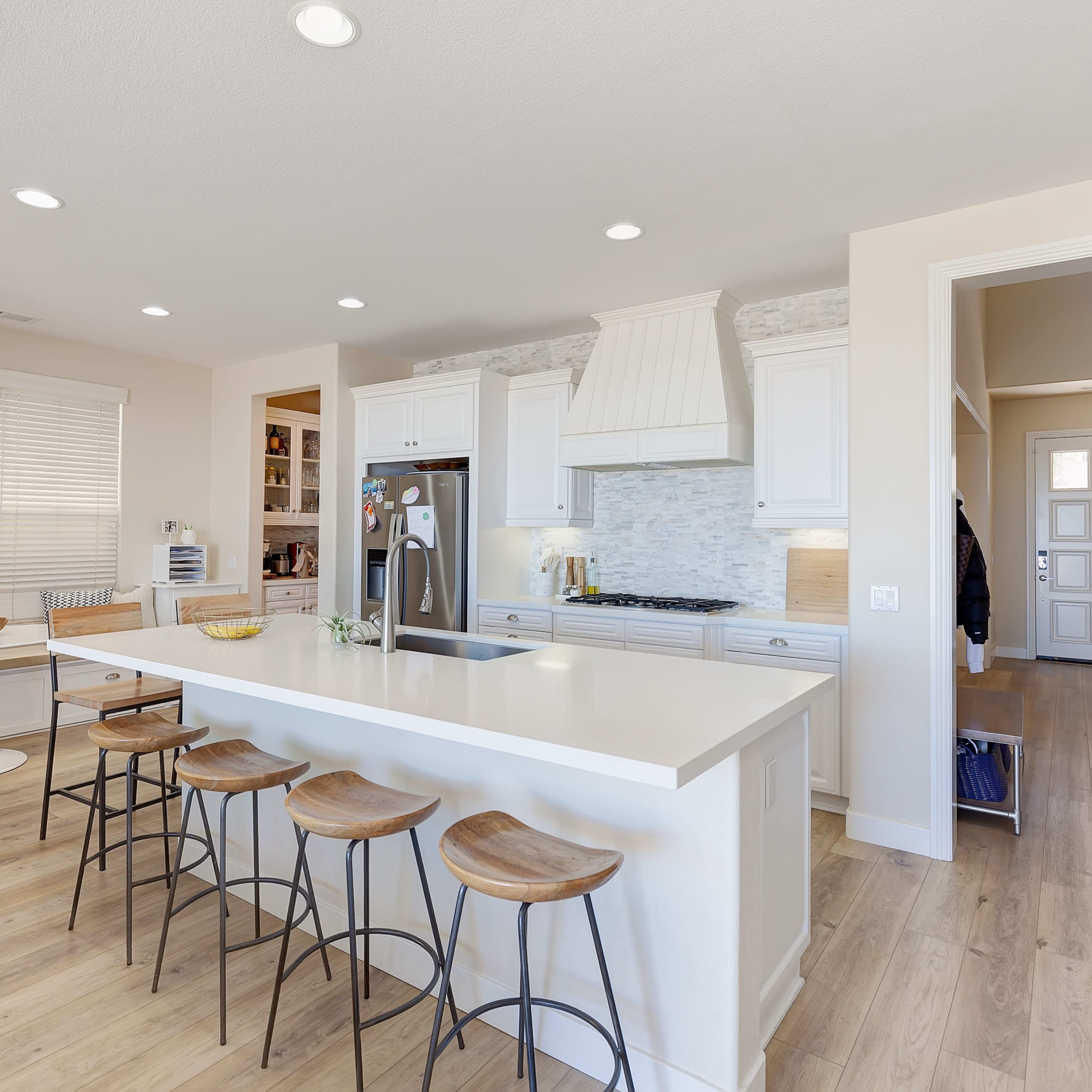 A modern kitchen with white cabinetry, a large island with bar stools, and a door leading to a hallway.