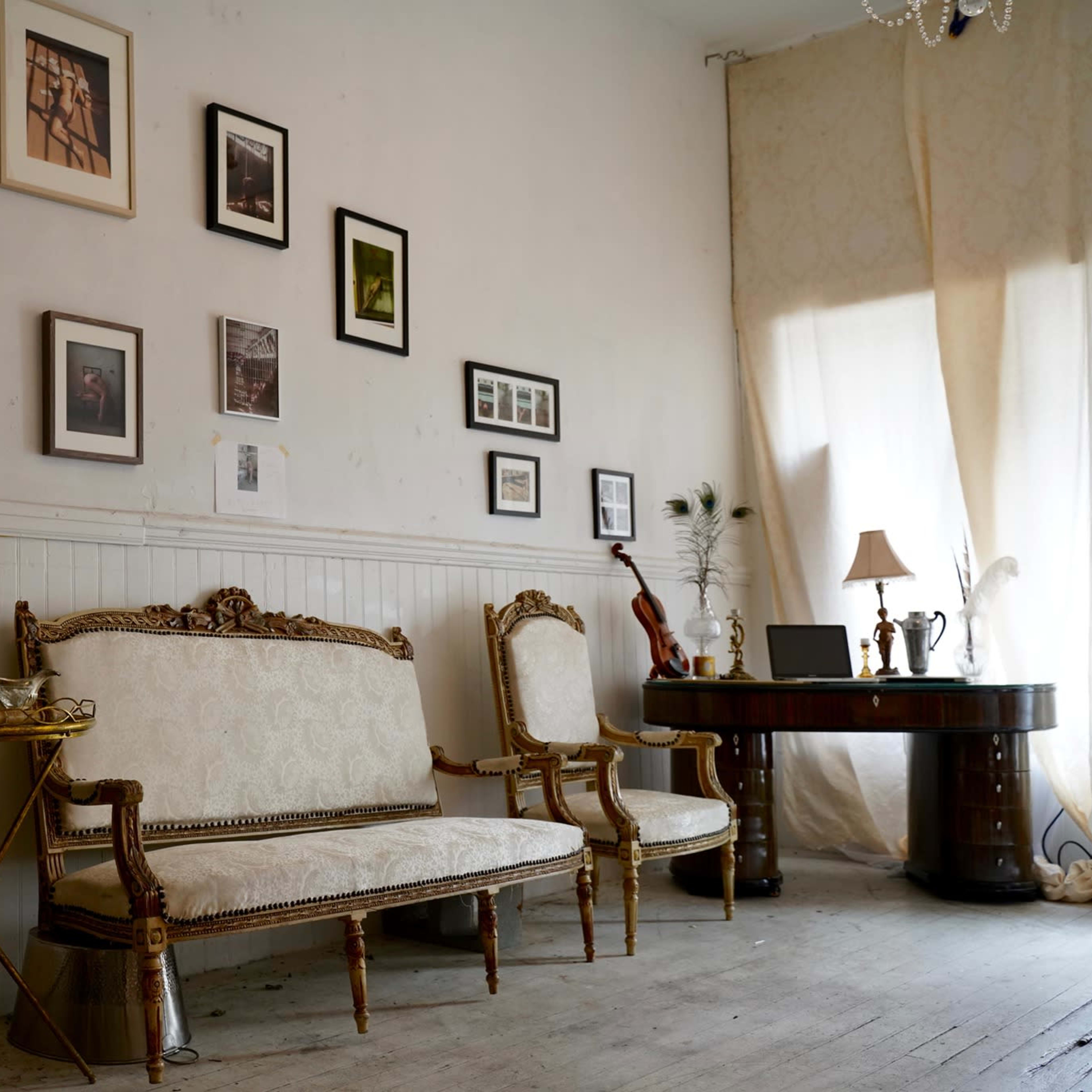 A bright room features elegant seating, a wooden table, and a wall adorned with framed photographs.