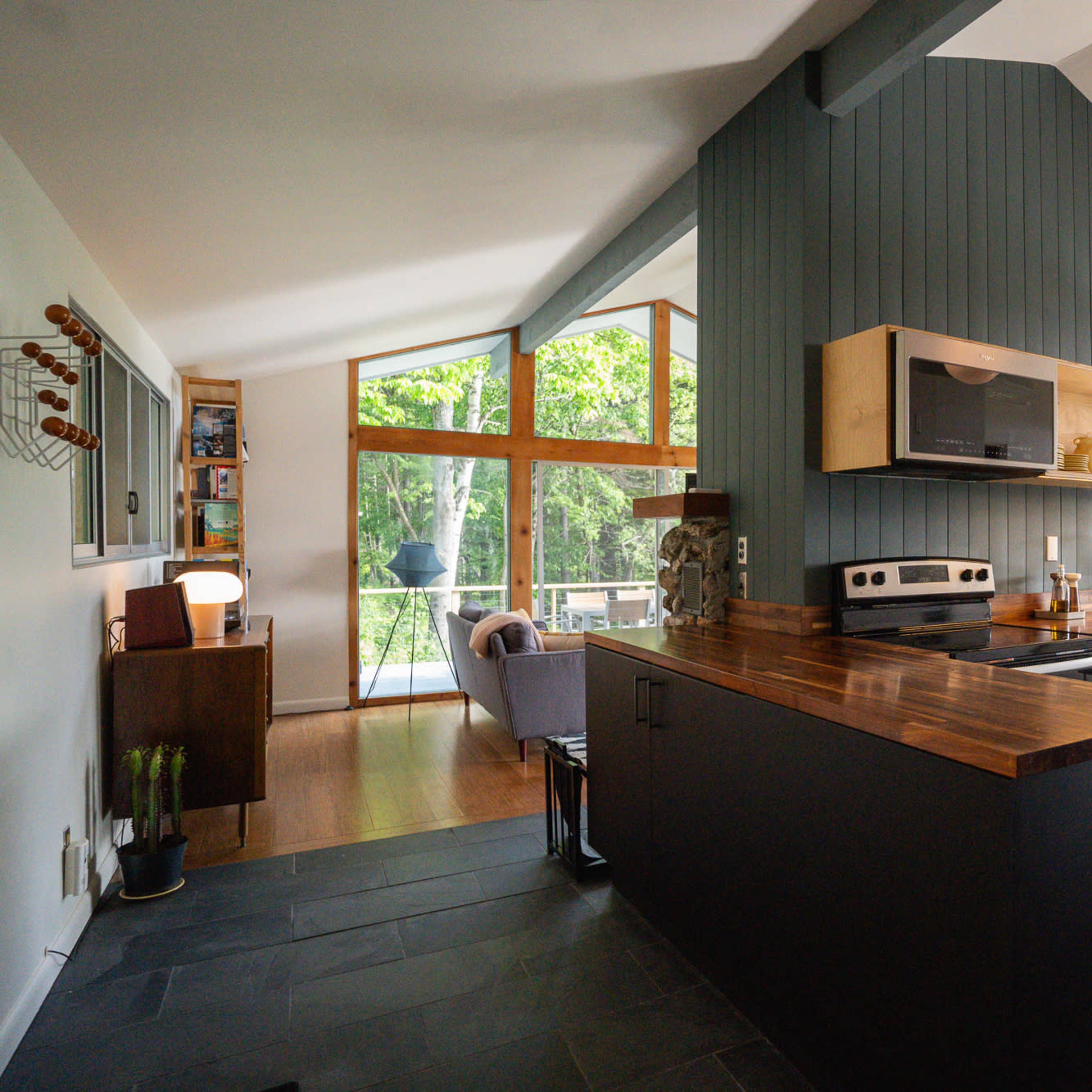 A modern kitchen features dark cabinetry, a wooden countertop, and large windows that provide a view of the outdoors.