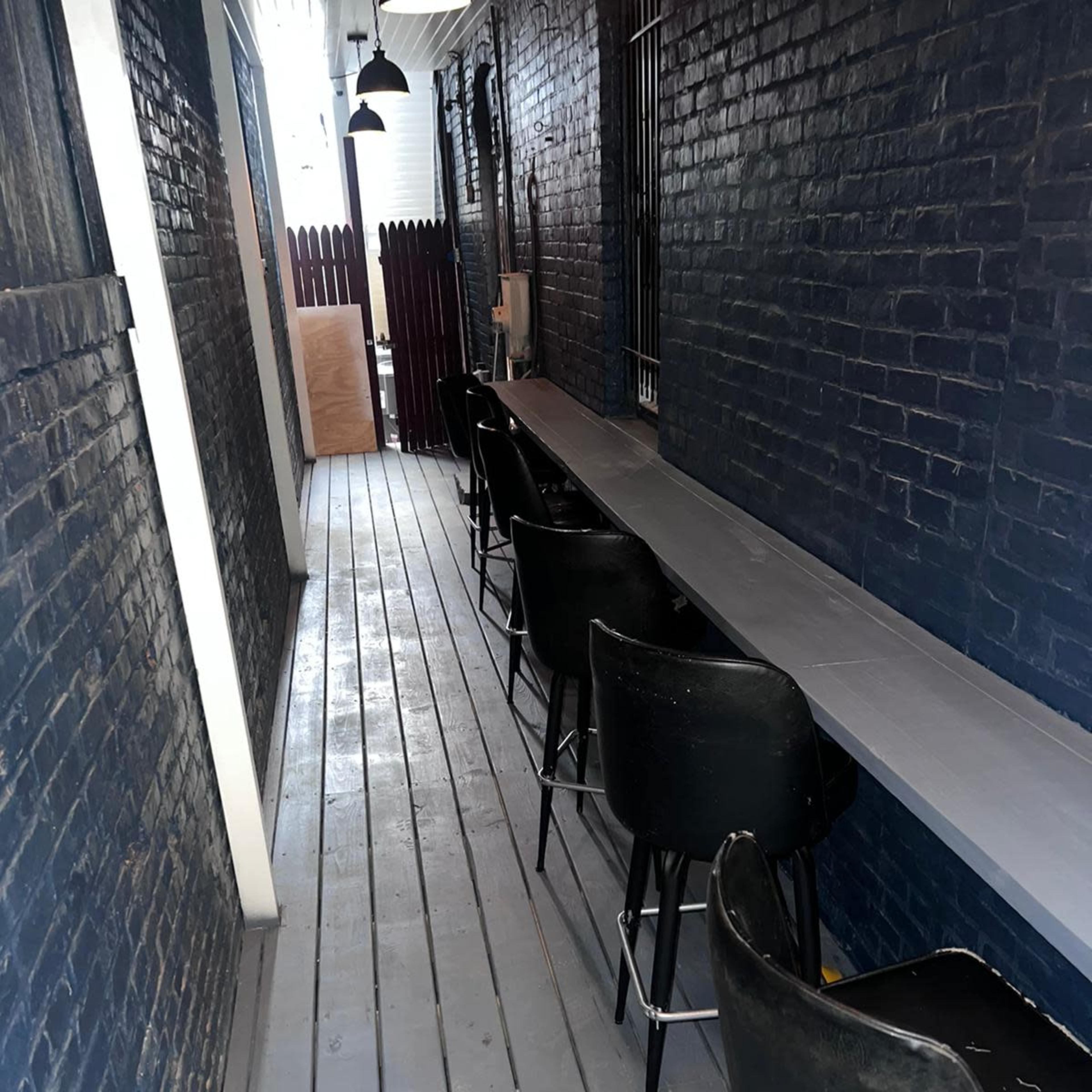 A narrow, dimly lit corridor with a row of black bar stools along a long gray counter against a dark brick wall.