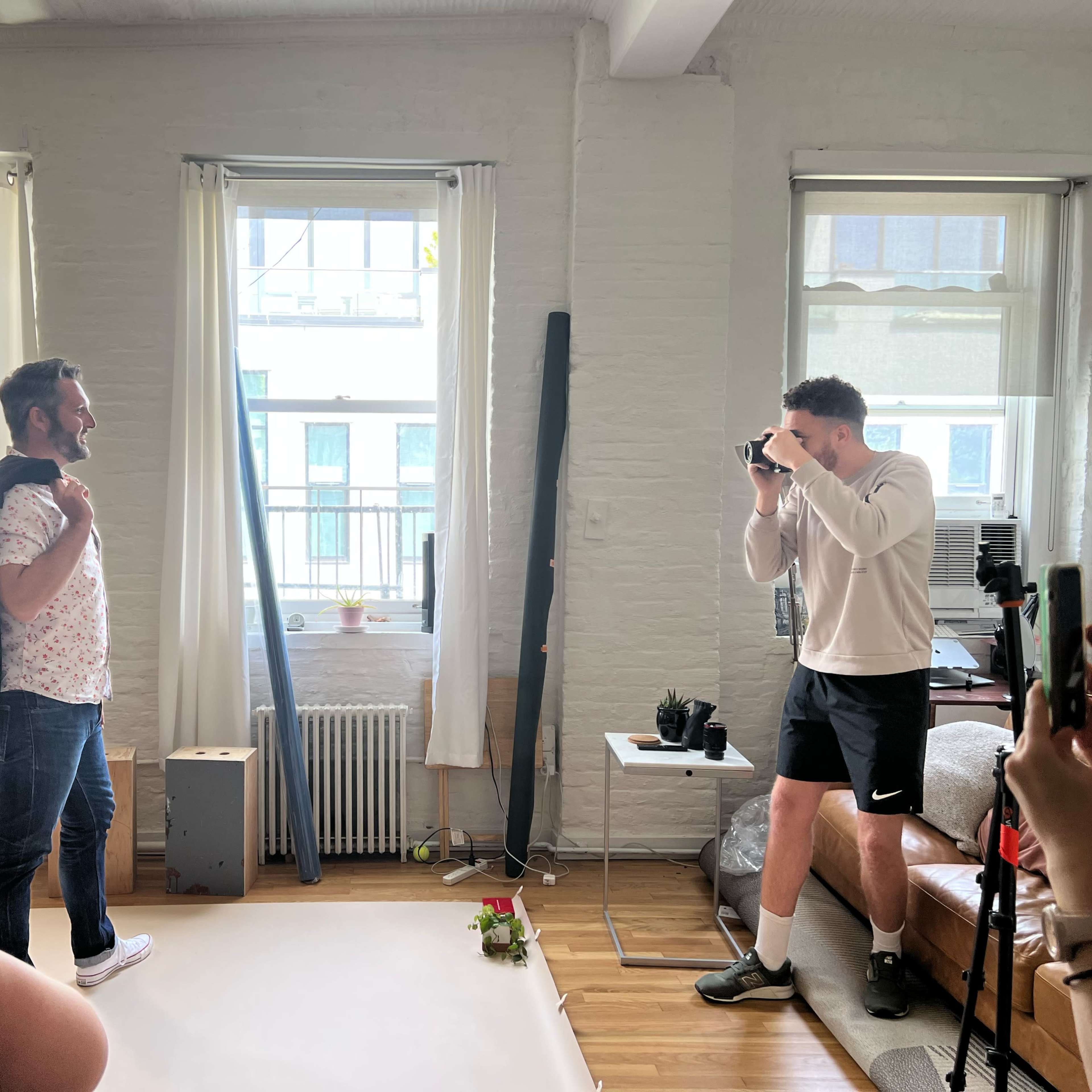 Two people are in a bright, minimalistic studio setting, with one person posing for a photo while the other takes the picture.
