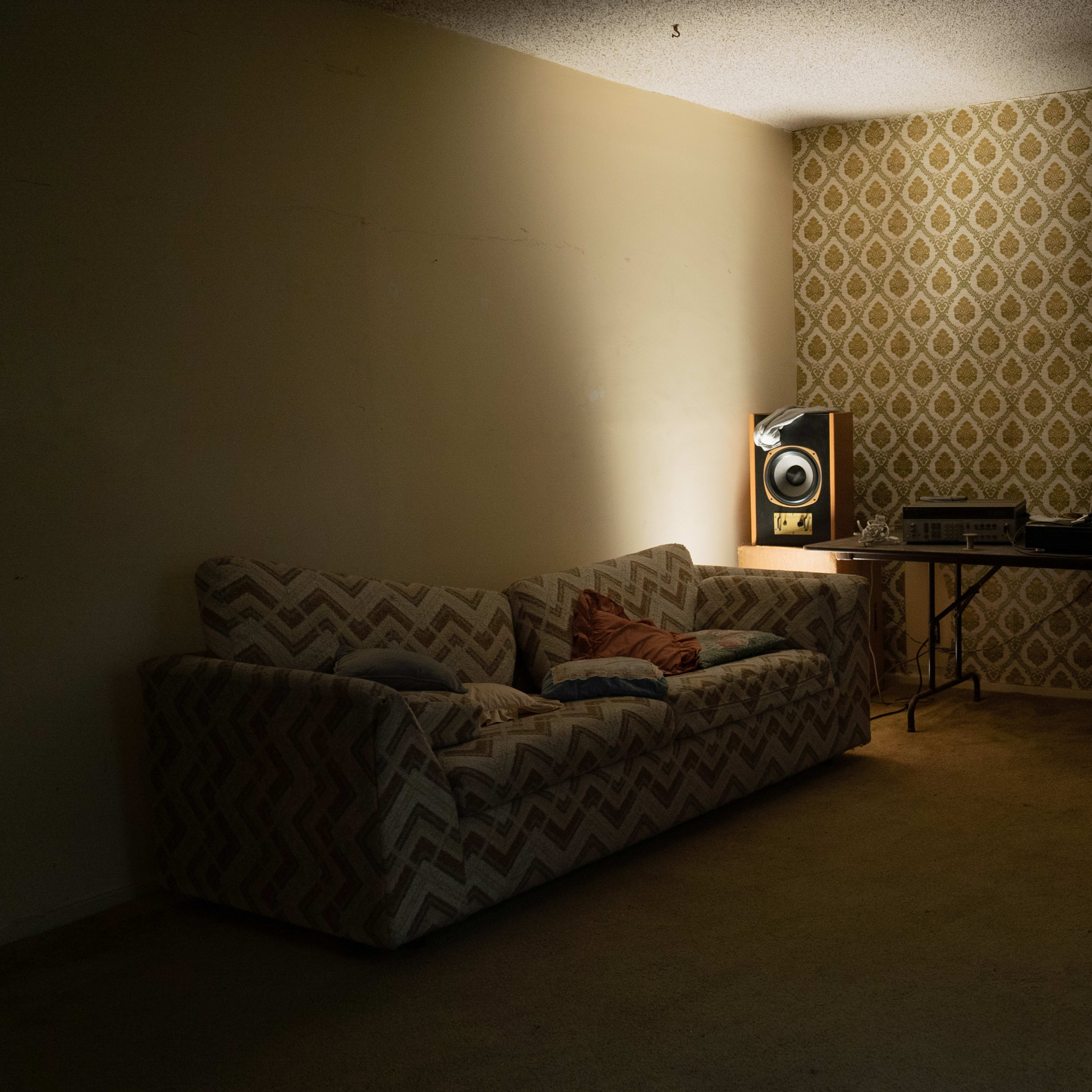 A dimly lit room with a patterned wallpaper, a sofa, and a table featuring audio equipment and speakers.