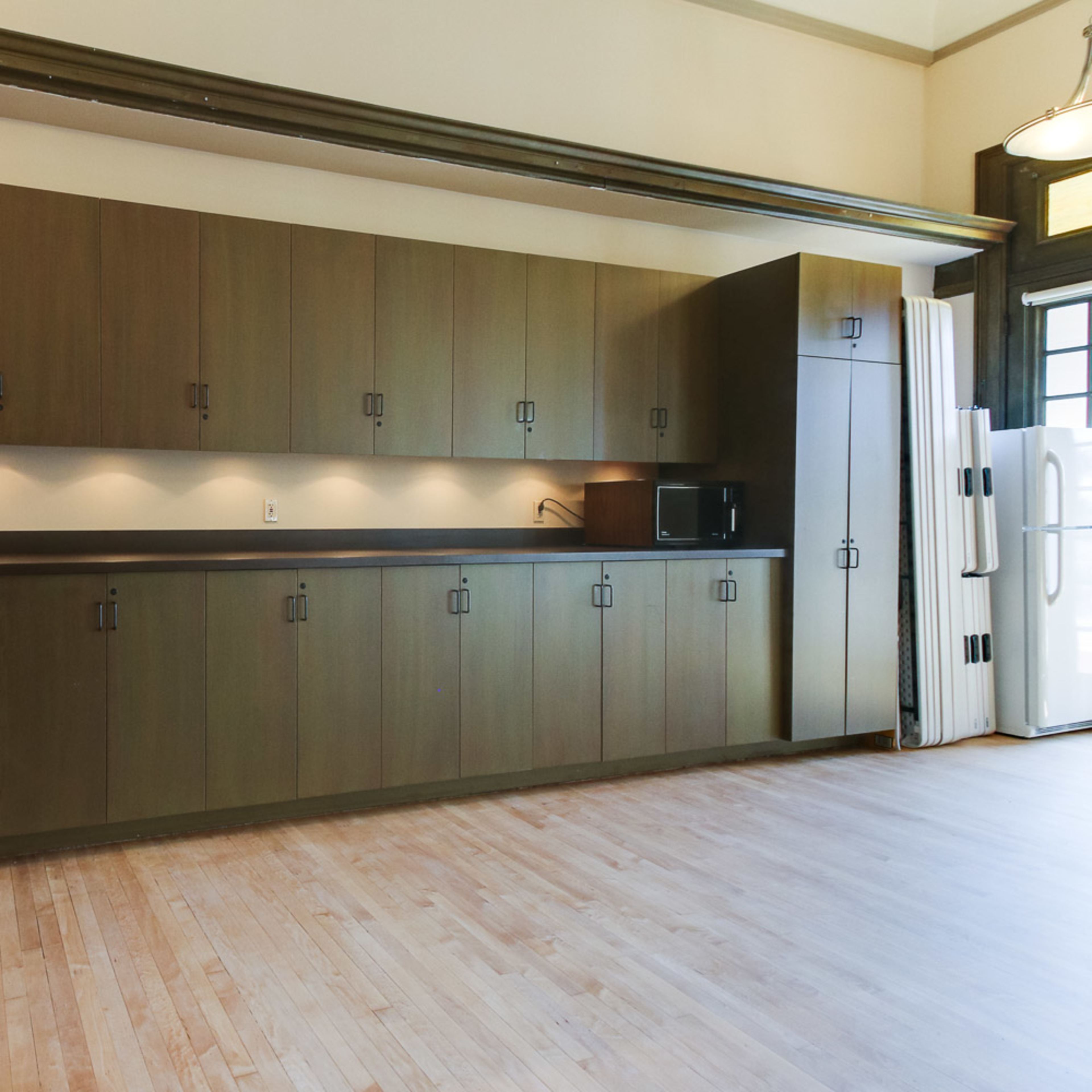 A spacious kitchen with dark wooden cabinetry, a light-colored countertop, and a white under-counter refrigerator.