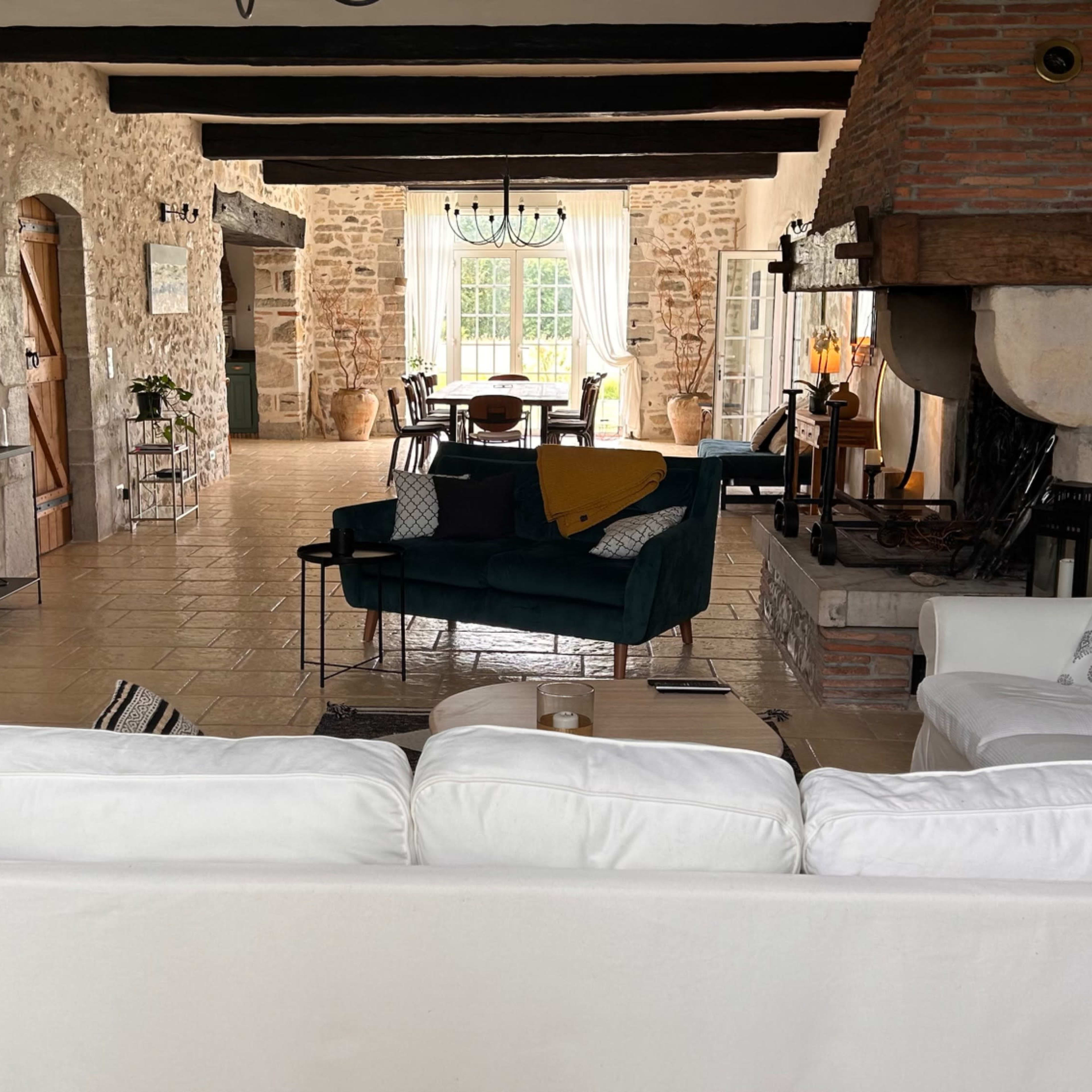 A spacious, rustic living area with stone walls, wooden beams, and a cozy seating arrangement centered around a fireplace.