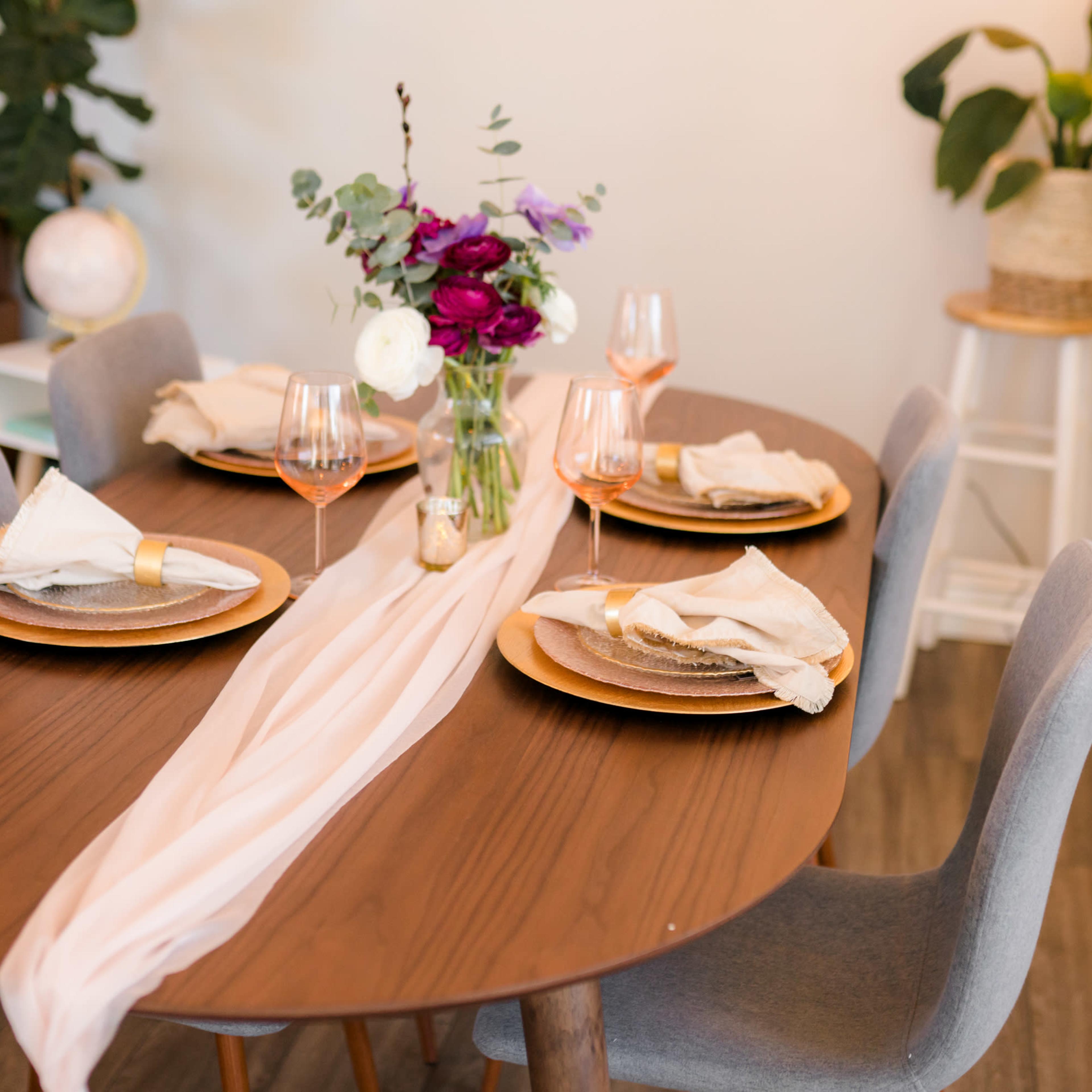 A neatly set dining table features a floral centerpiece and elegant dinnerware against a backdrop of a cozy living space.