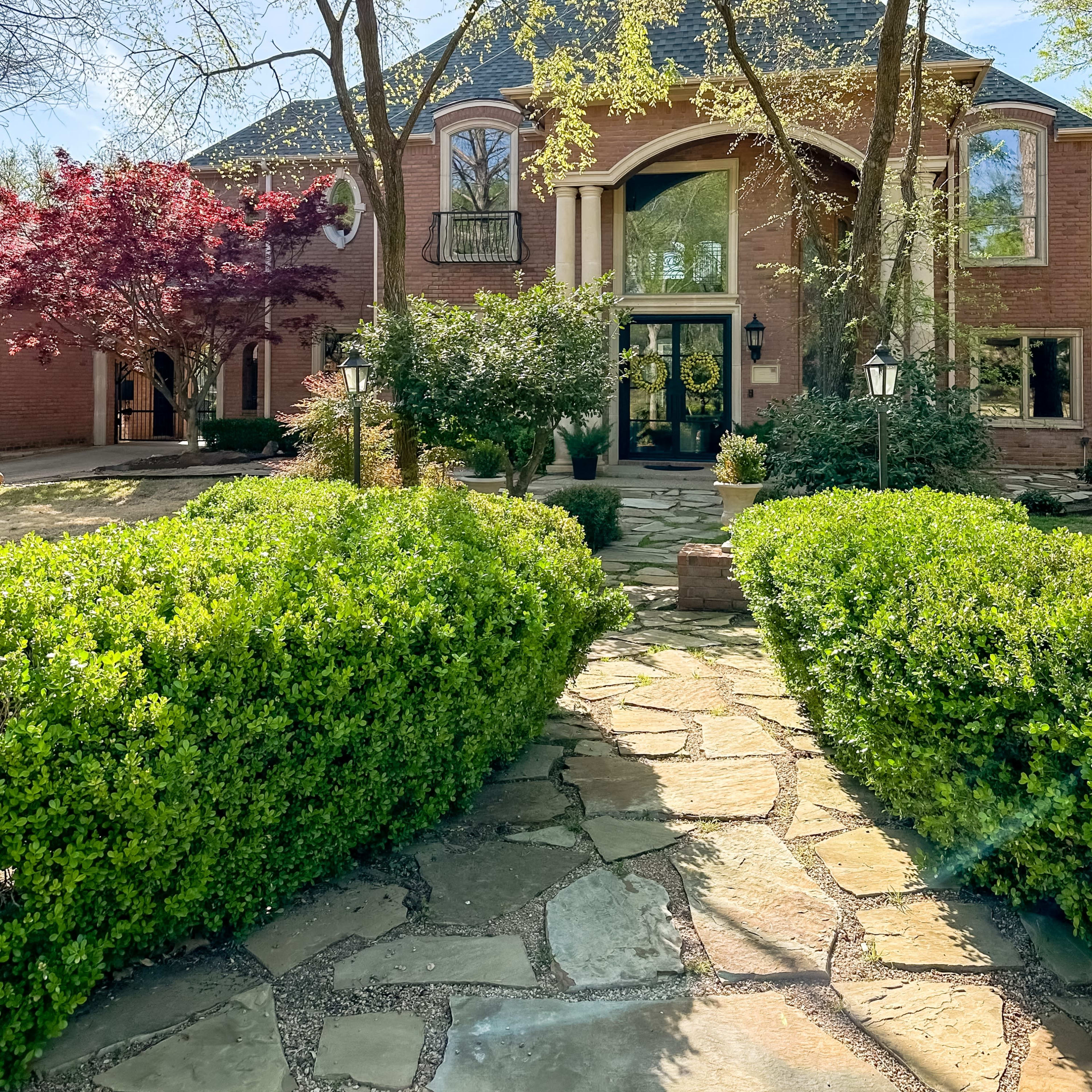 A large brick house with a steeply pitched roof is surrounded by well-maintained landscaping and trees.