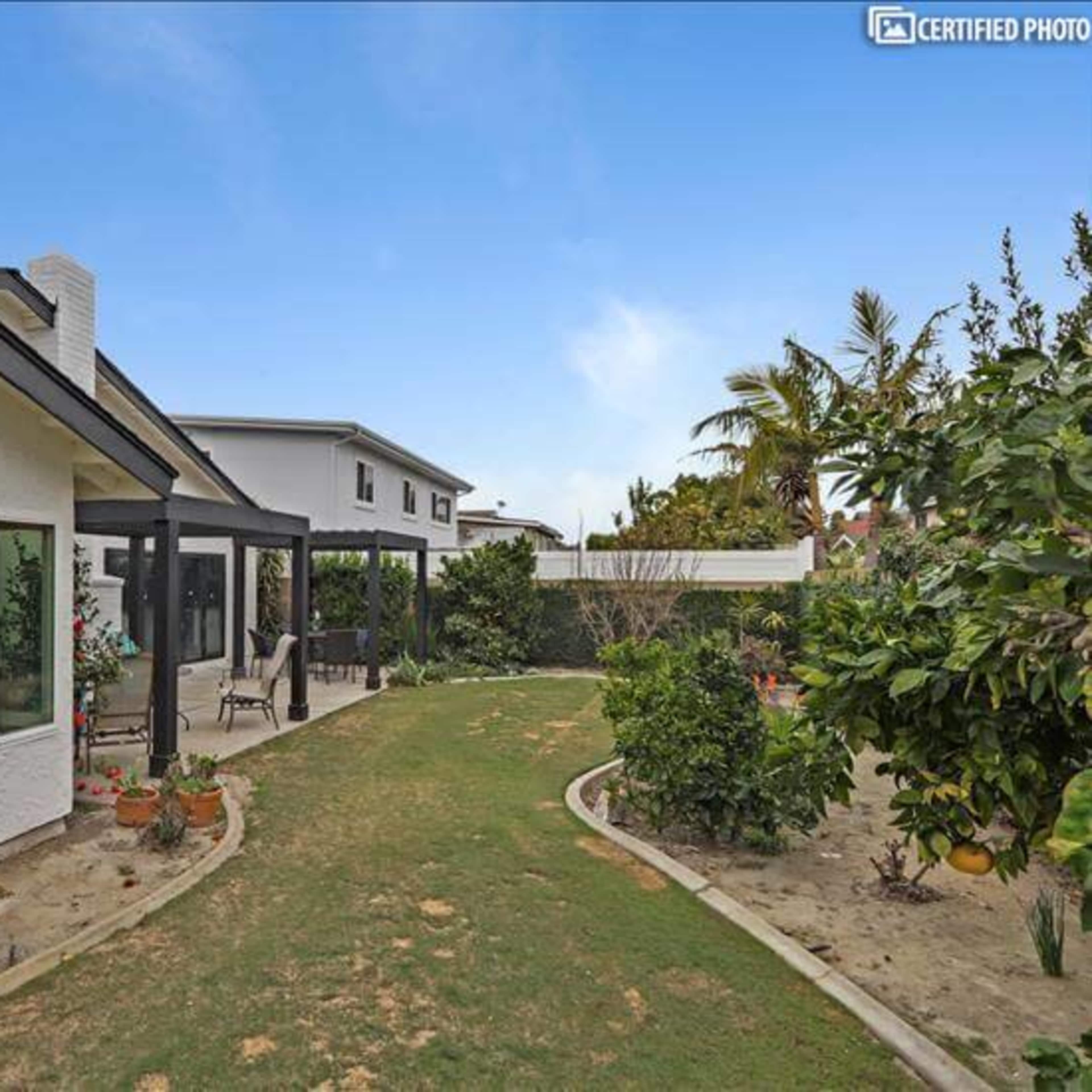 A landscaped pathway between two houses, bordered by various plants and trees.