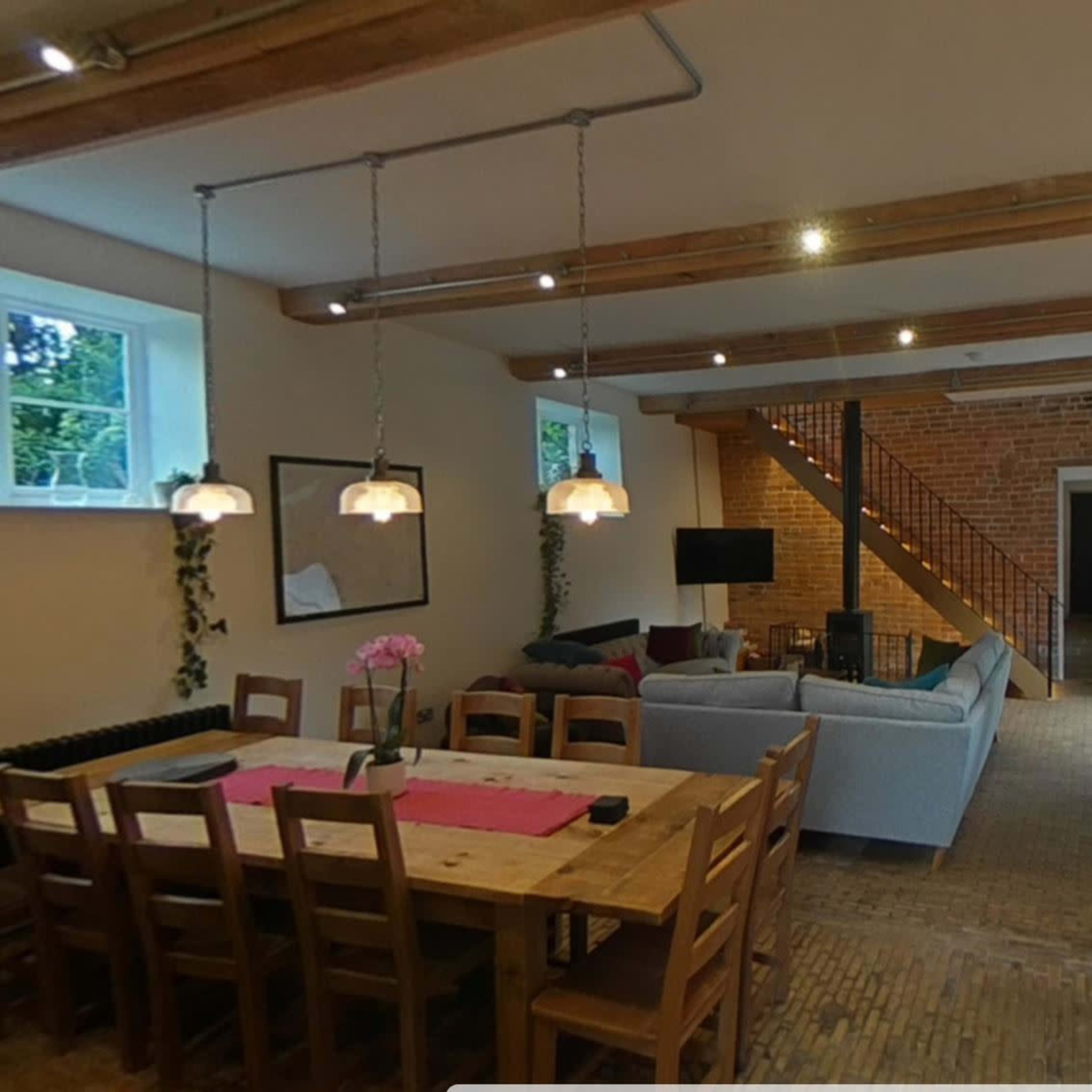 A modern interior space featuring a dining area with a wooden table and chairs, a living area with a sofa and television, and a staircase made of wood.