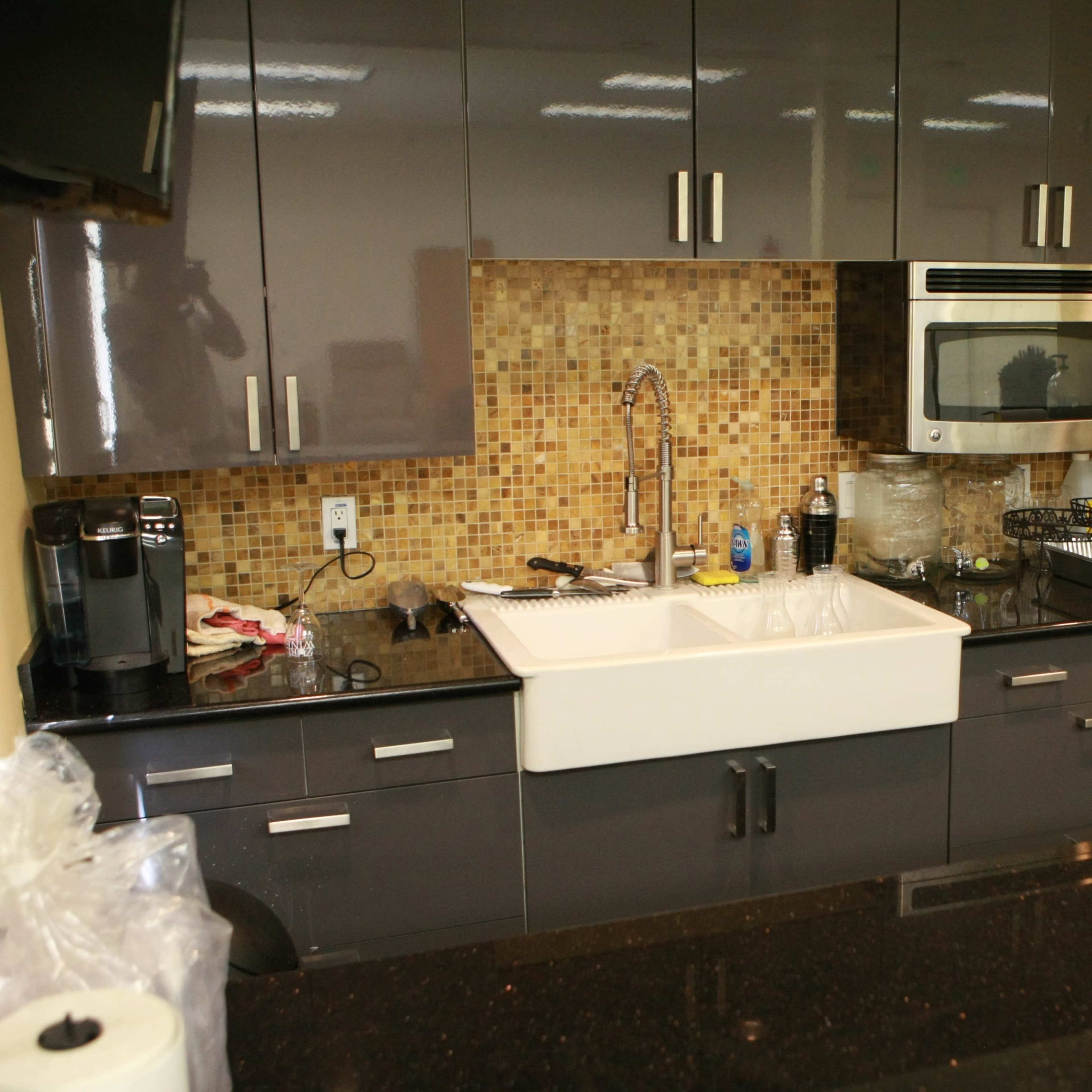 A modern kitchen with dark cabinets, a double sink, stainless steel appliances, and a mosaic backsplash.