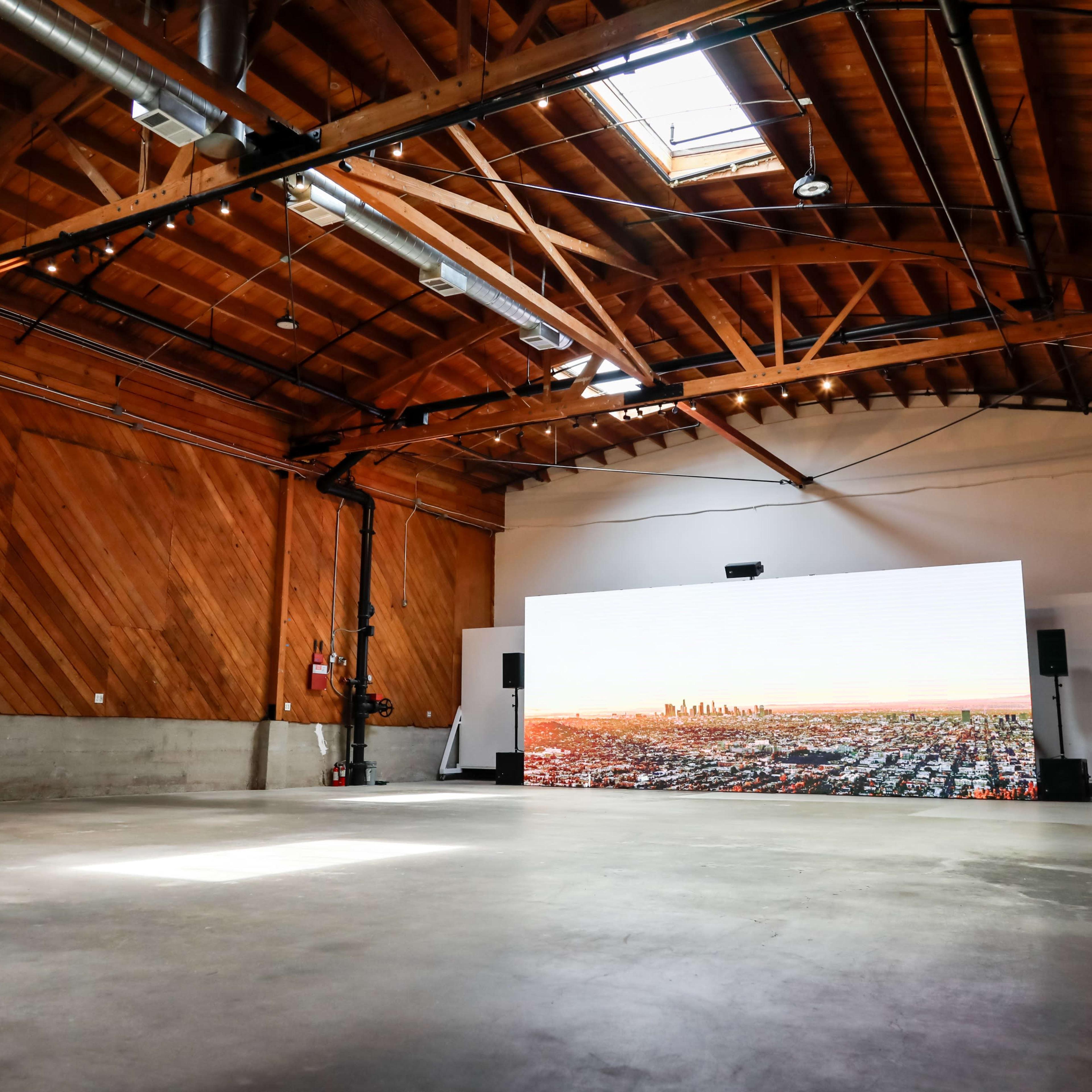 A spacious room with wooden beams features a large video screen displaying a city skyline.