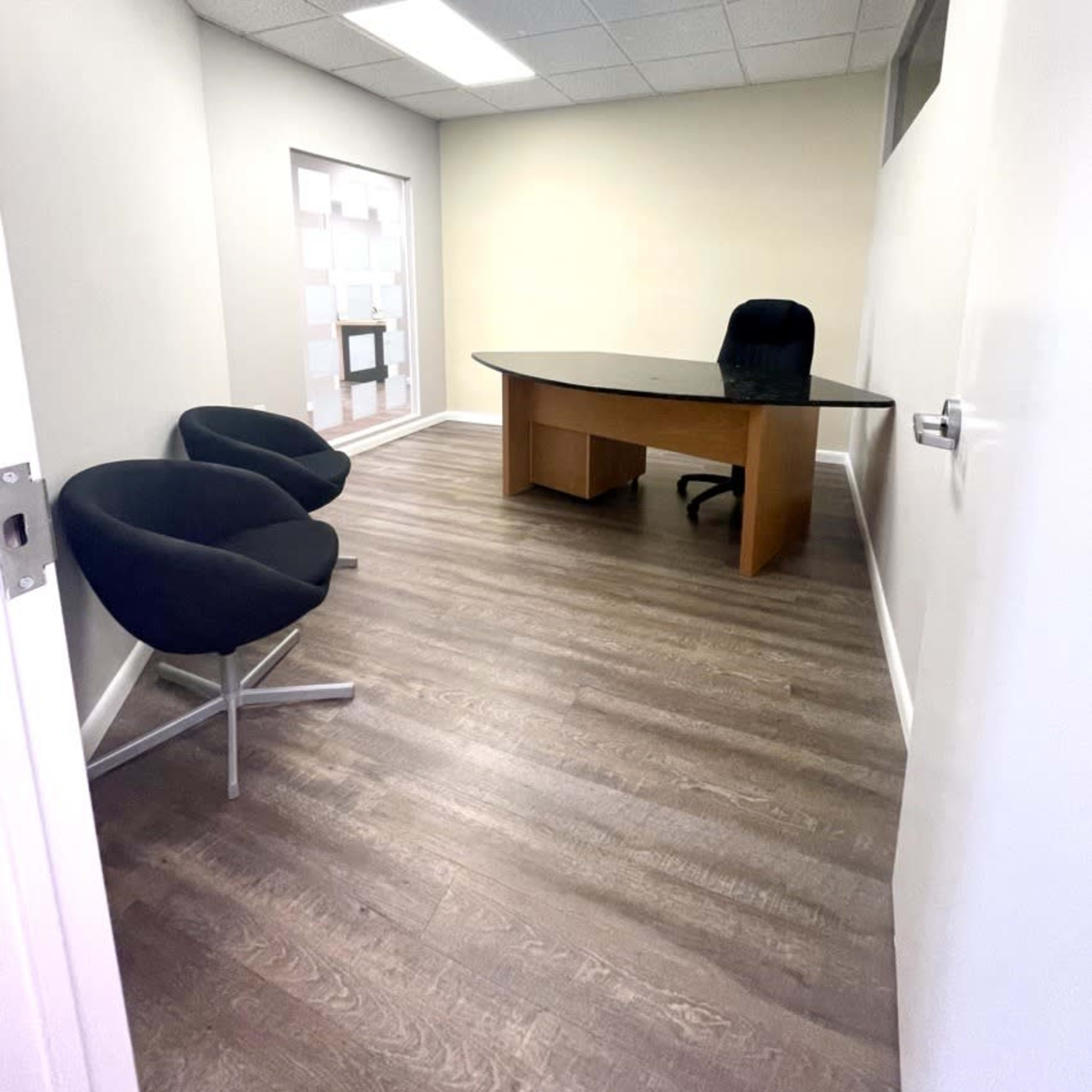 A small office space featuring a wooden desk, a black office chair, and two black chairs against the walls.