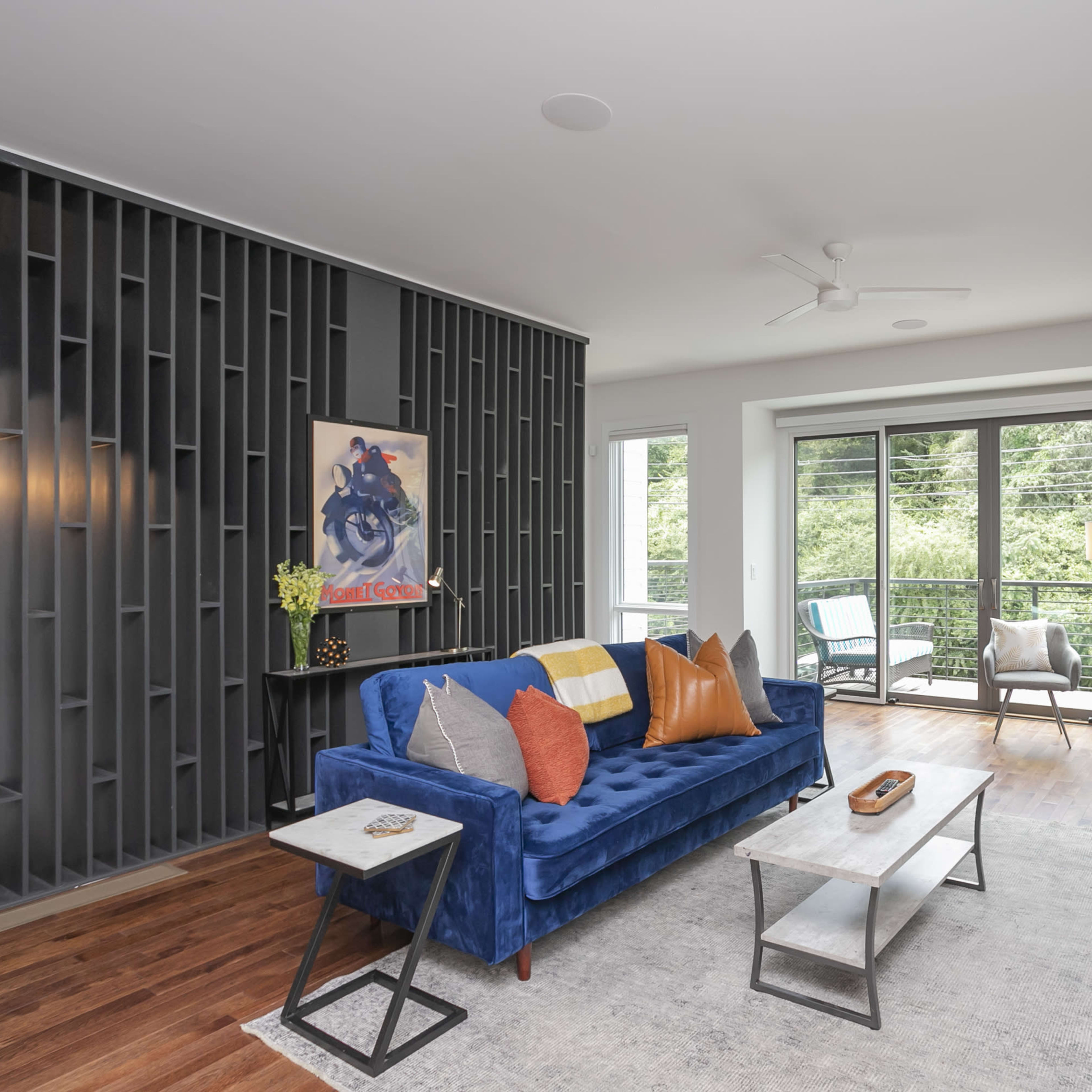 A modern living room features a blue sofa, a gray coffee table, and large windows overlooking a green landscape.