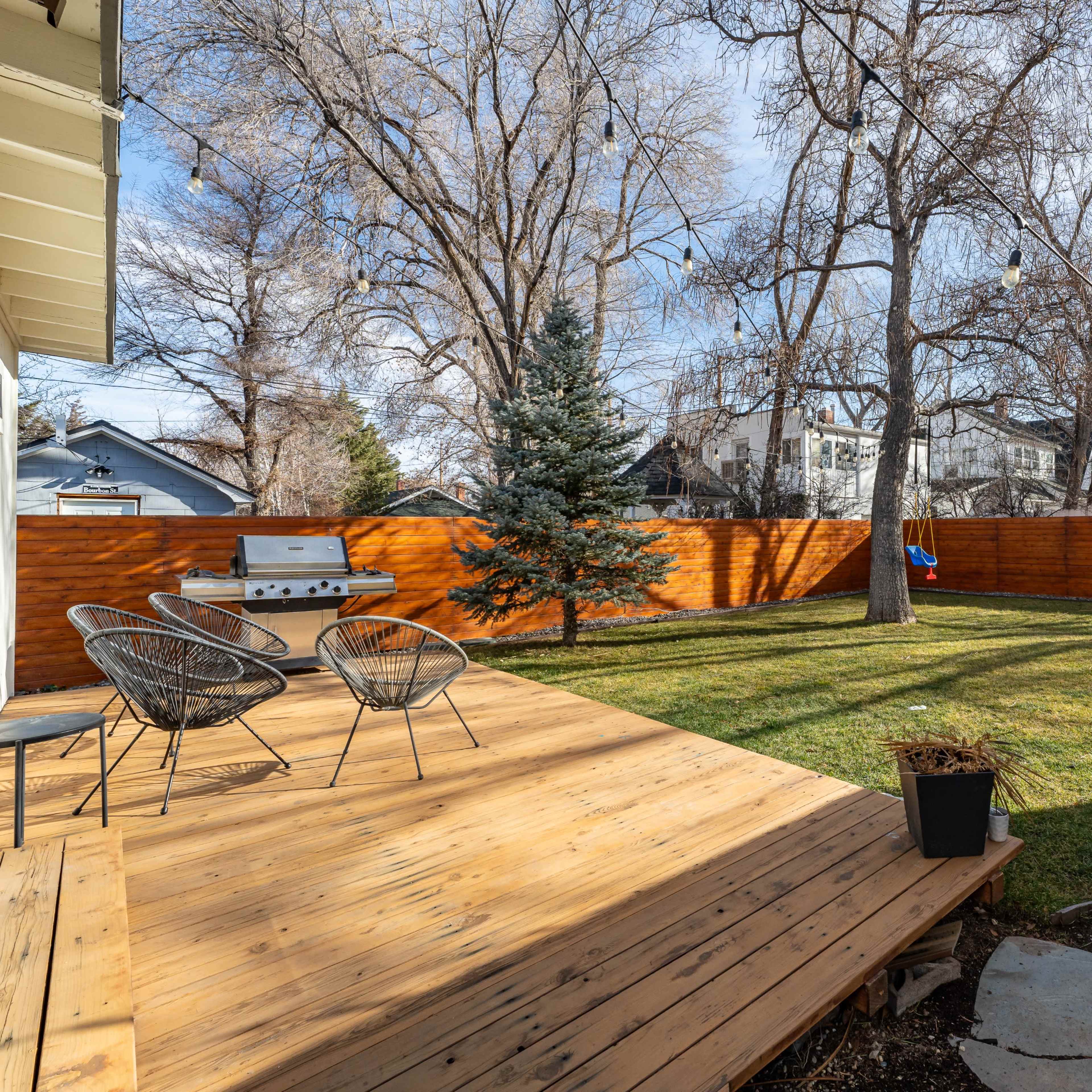 A wooden deck with two chairs overlooks a grassy backyard bordered by a wooden fence and trees.