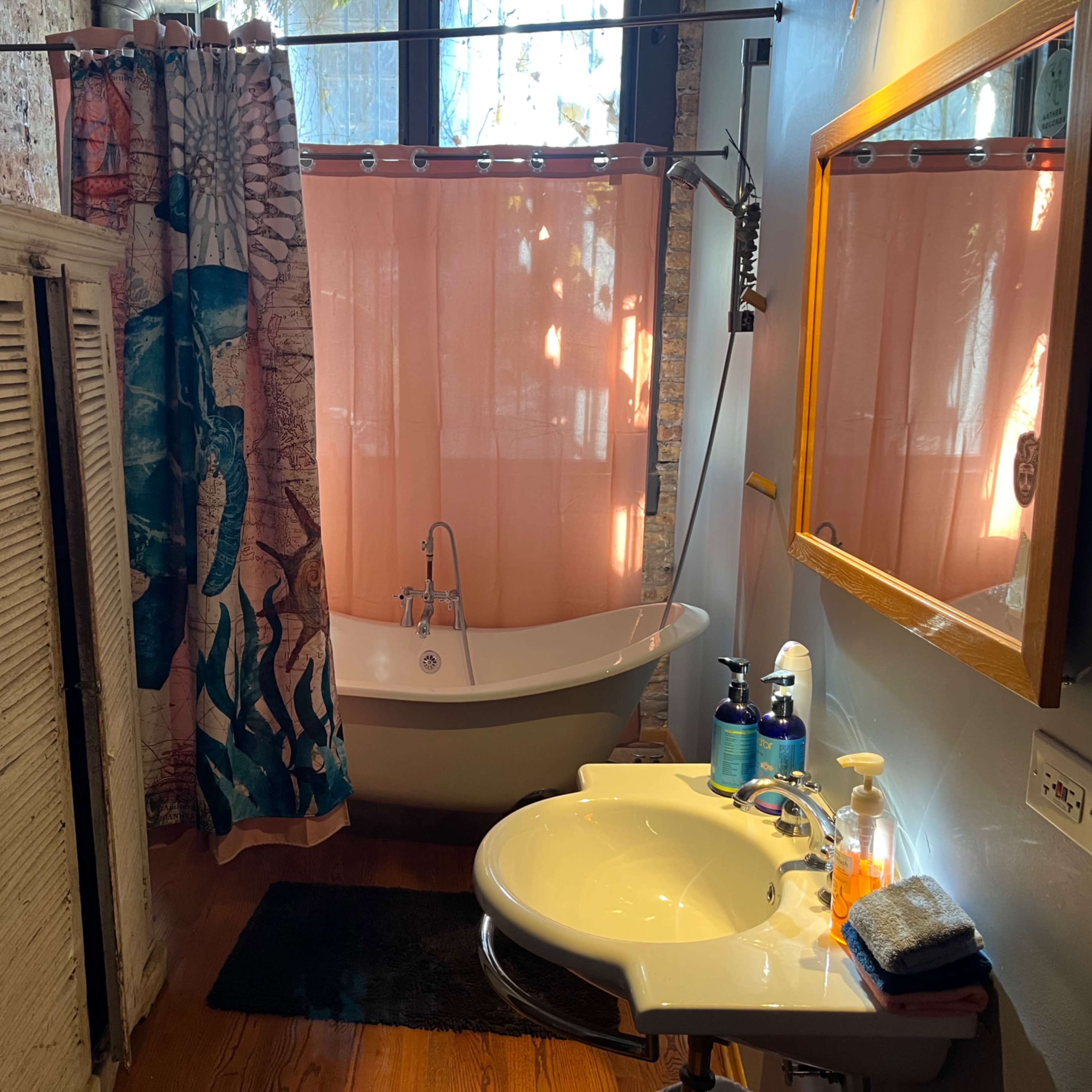 The bathroom features a freestanding bathtub, a pink shower curtain, a sink with toiletries, and a wooden cabinet against the wall.