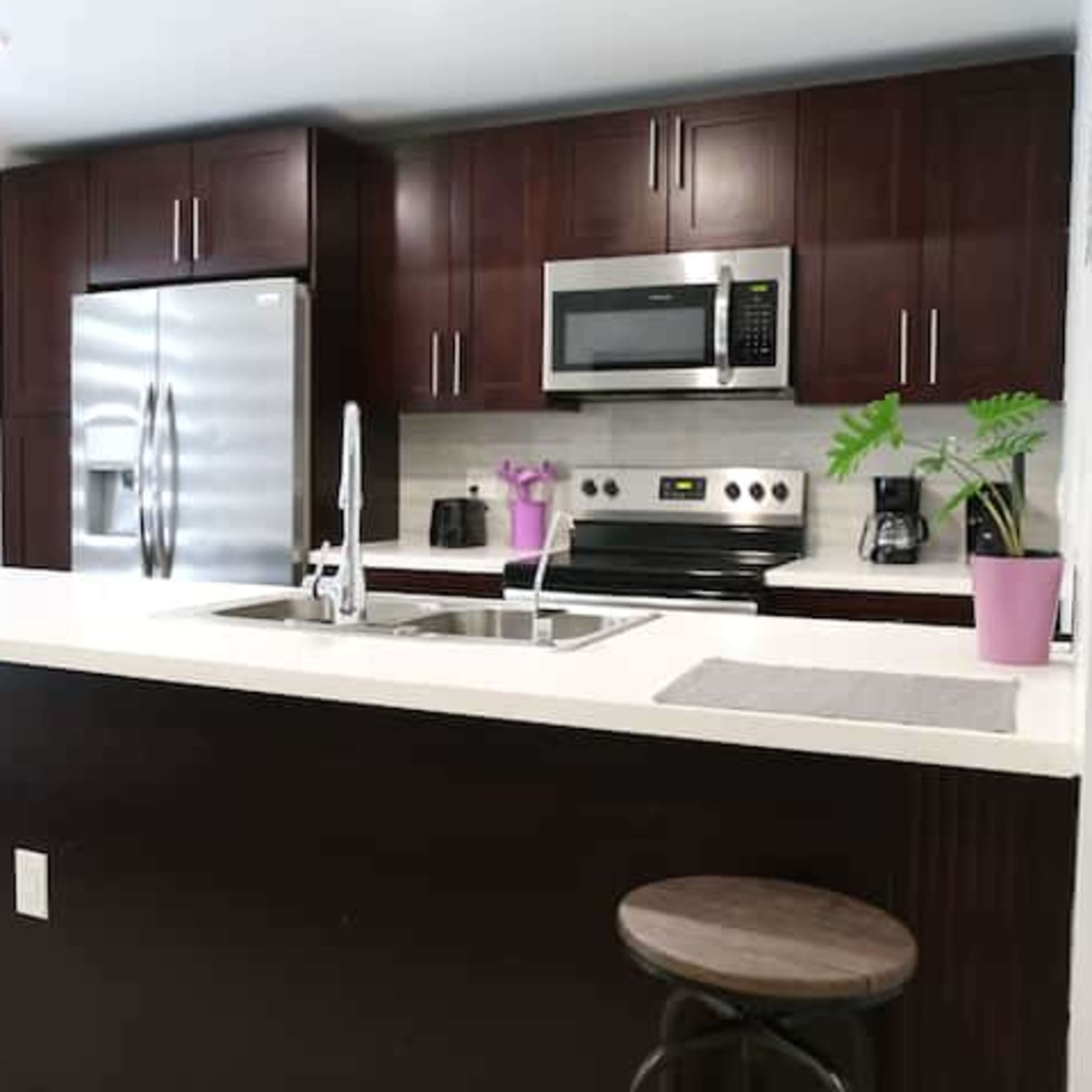 A modern kitchen features dark wood cabinetry, stainless steel appliances, and a central island with bar stools.