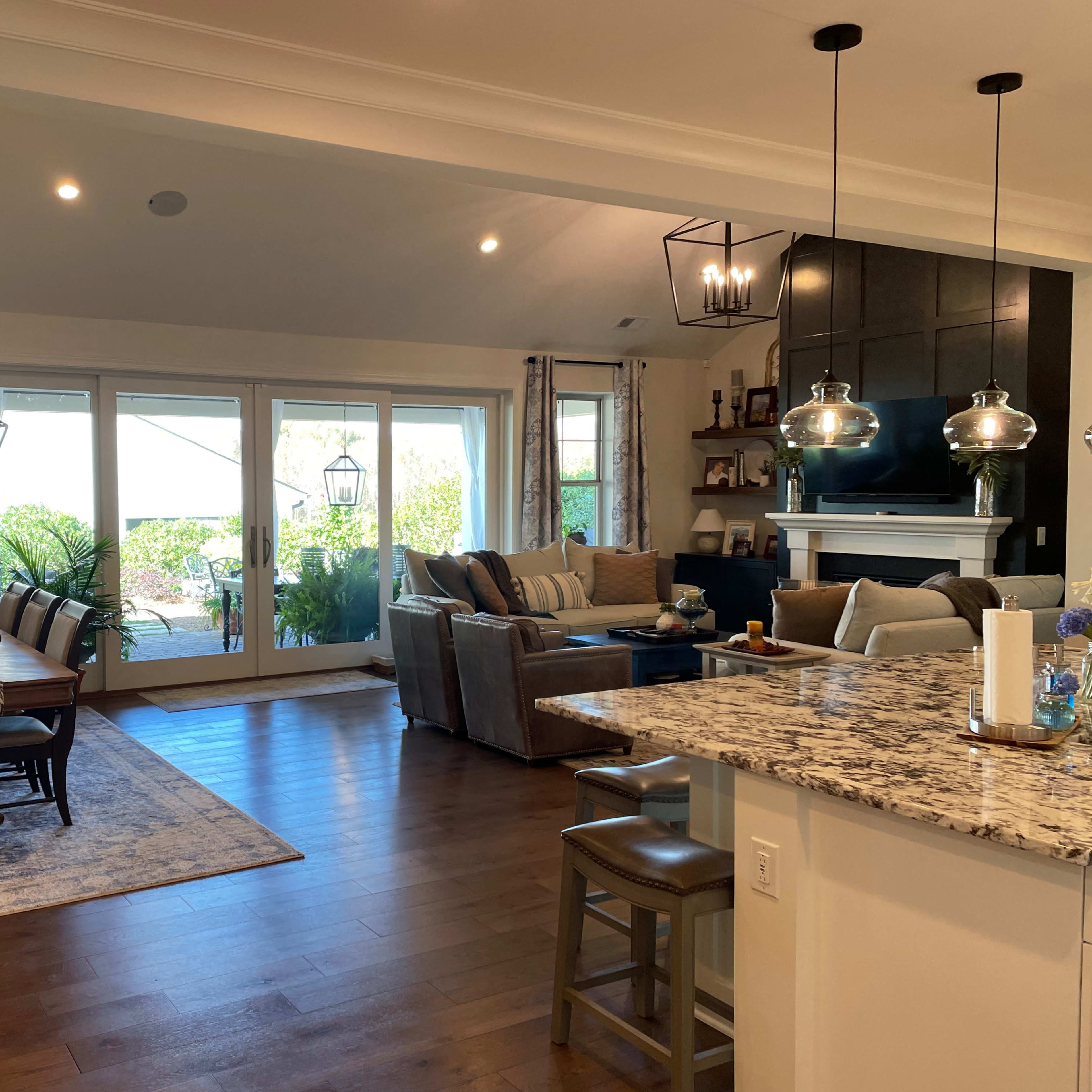 A modern open-concept living space with a dining area, kitchen, and sitting area, featuring large windows and contemporary furnishings.