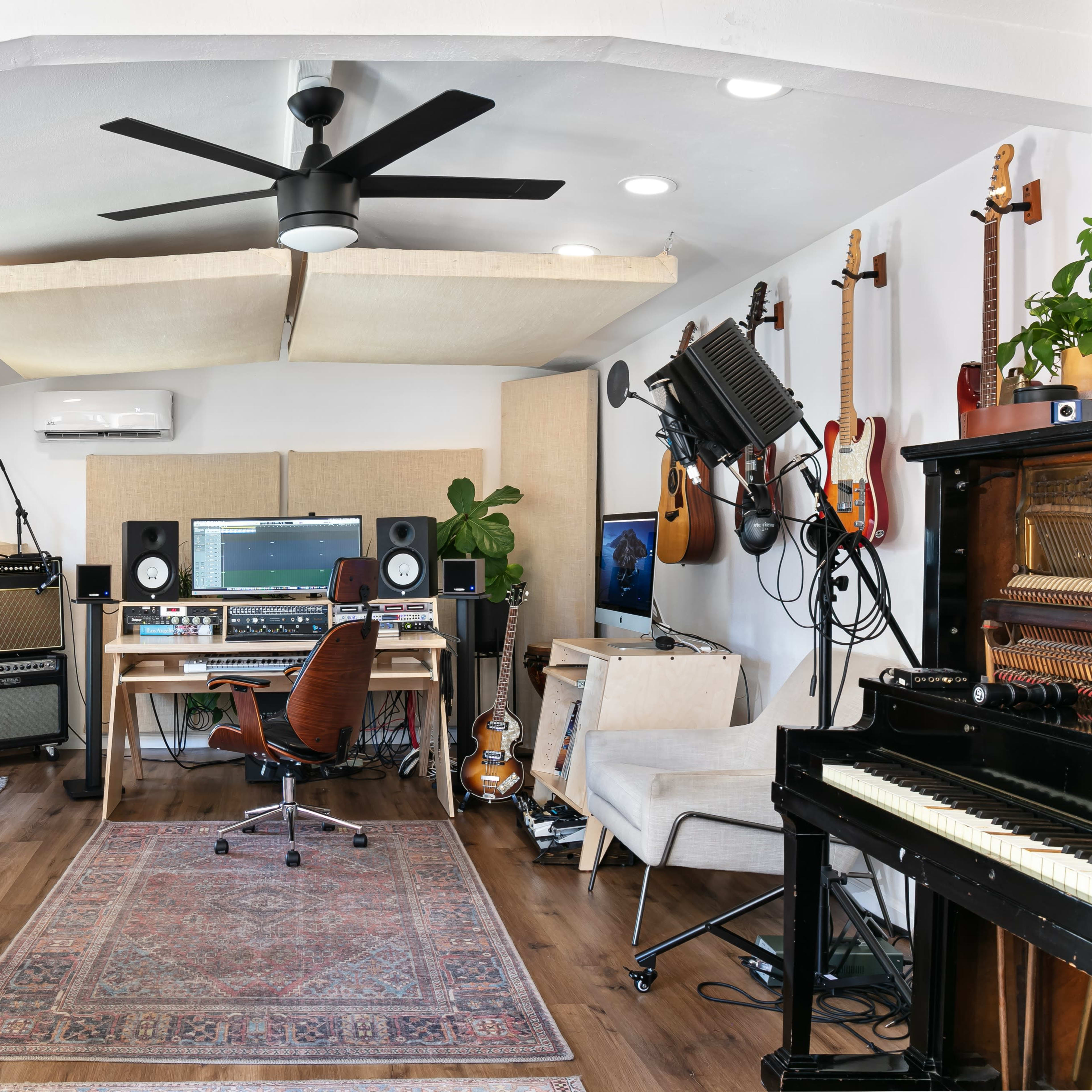 A home music studio featuring various instruments, a computer setup, and sound equipment arranged in a well-lit room with wood flooring.