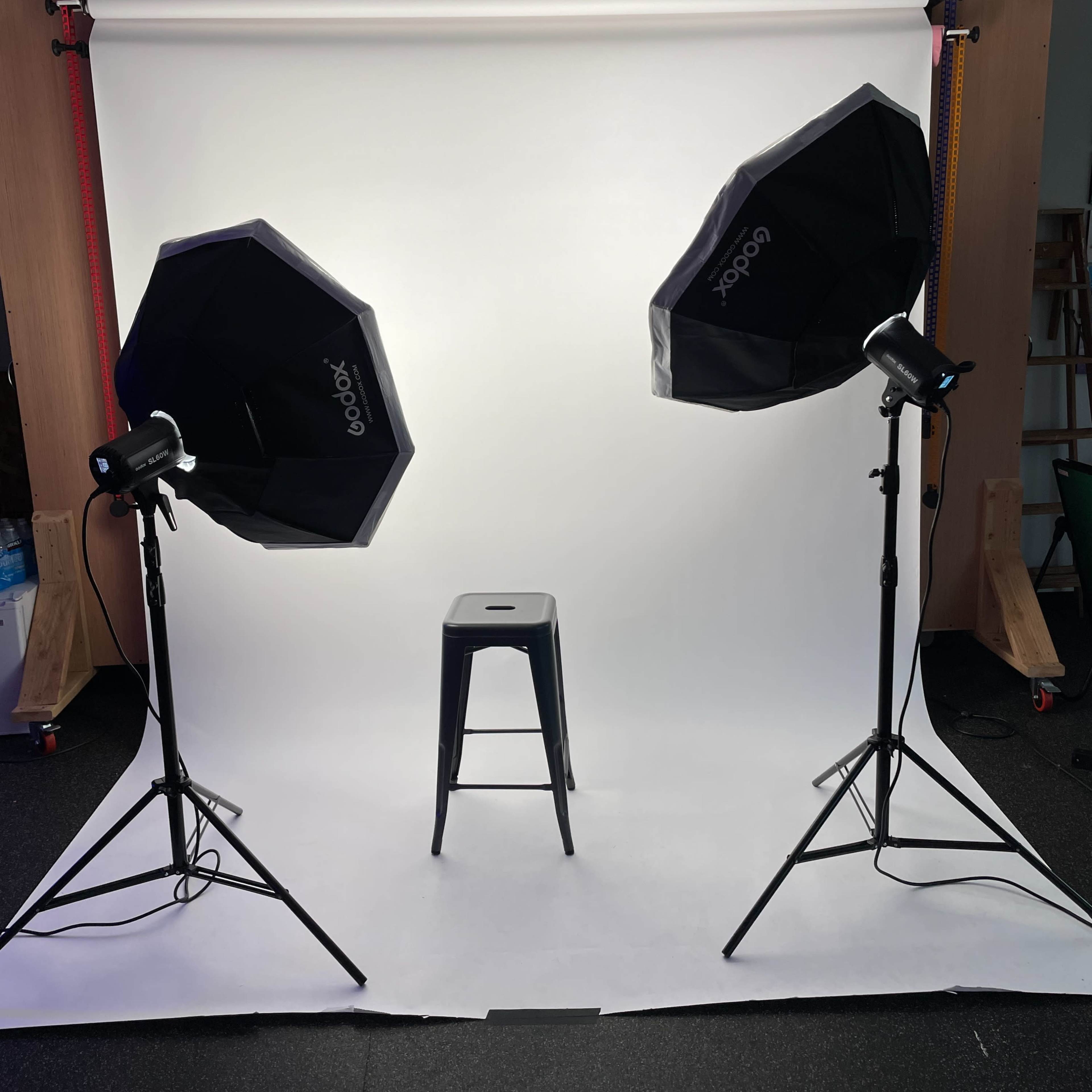 A black stool is positioned in front of a white backdrop lit by two softbox lights on either side.