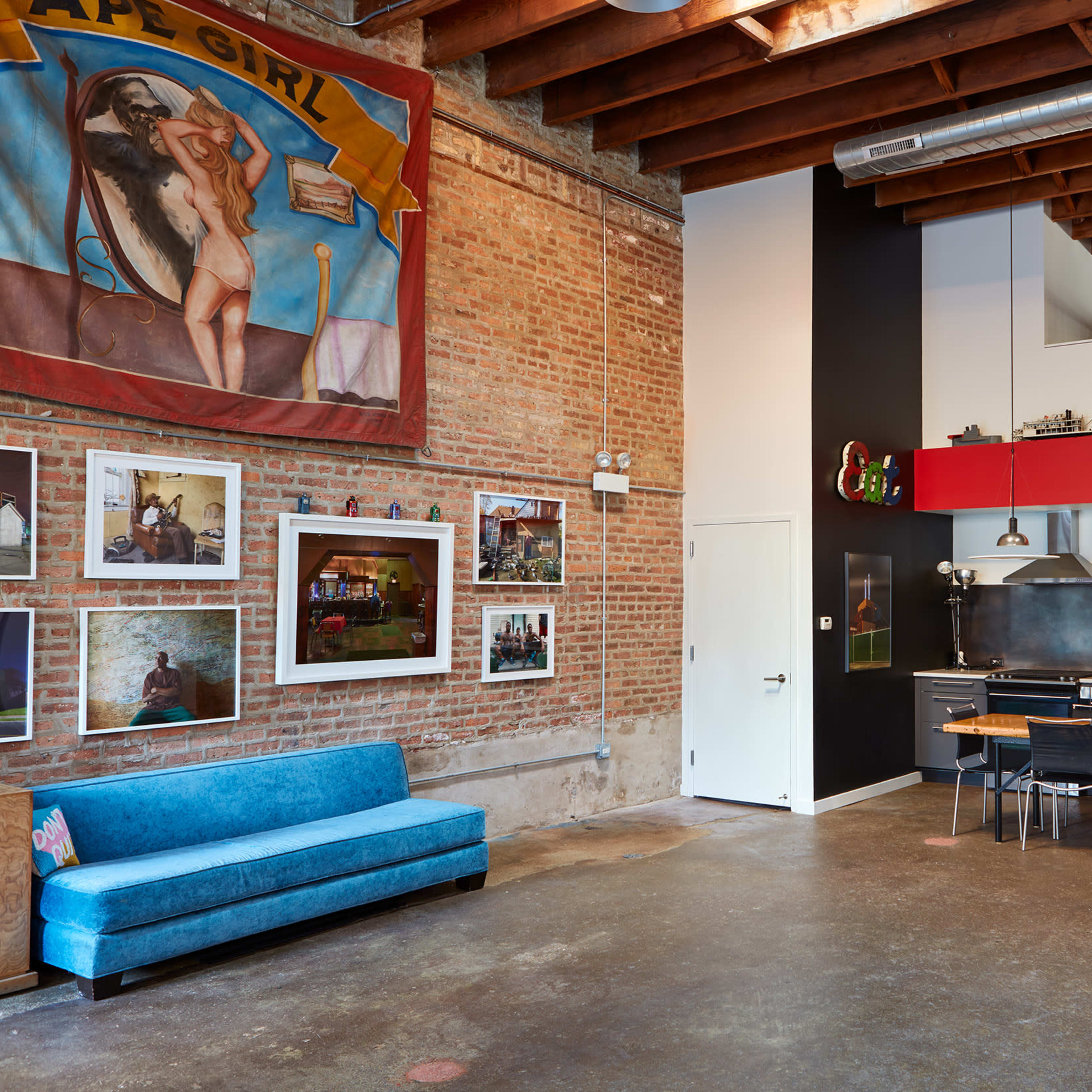 A spacious industrial-style kitchen and dining area with a brick wall, colorful artwork, and a long table surrounded by black chairs.
