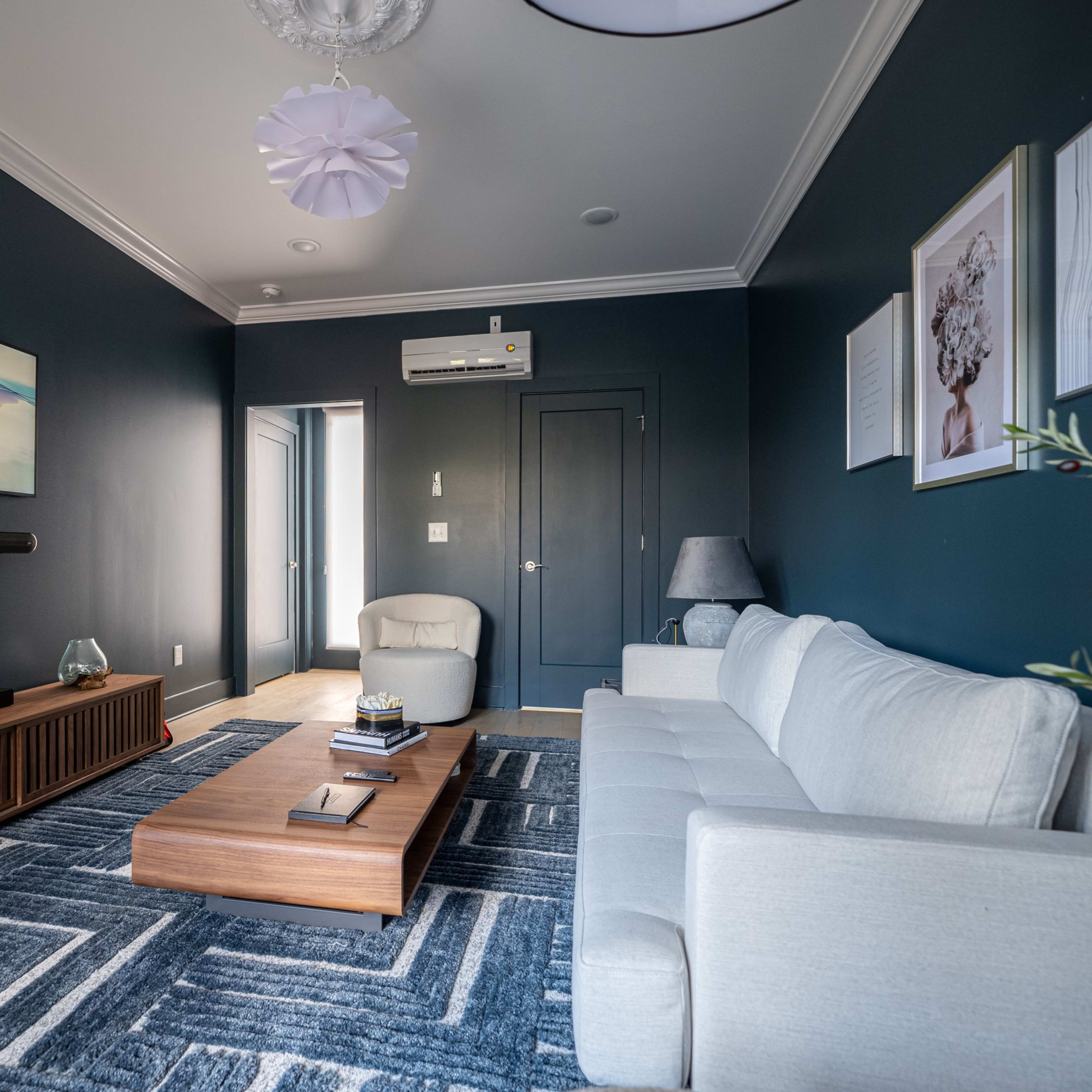 The living room features a gray sofa, a wooden coffee table, and a large wall-mounted television against a dark blue wall.