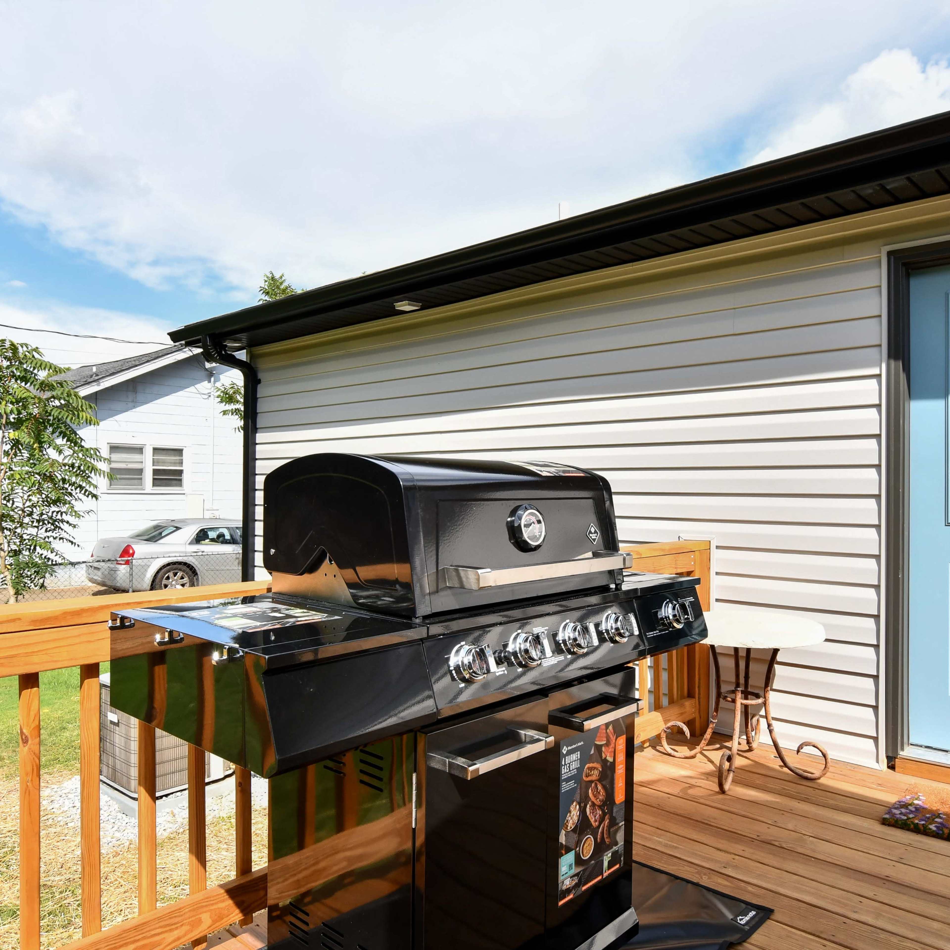 A black gas grill is positioned on a wooden deck next to a blue door leading into a house.