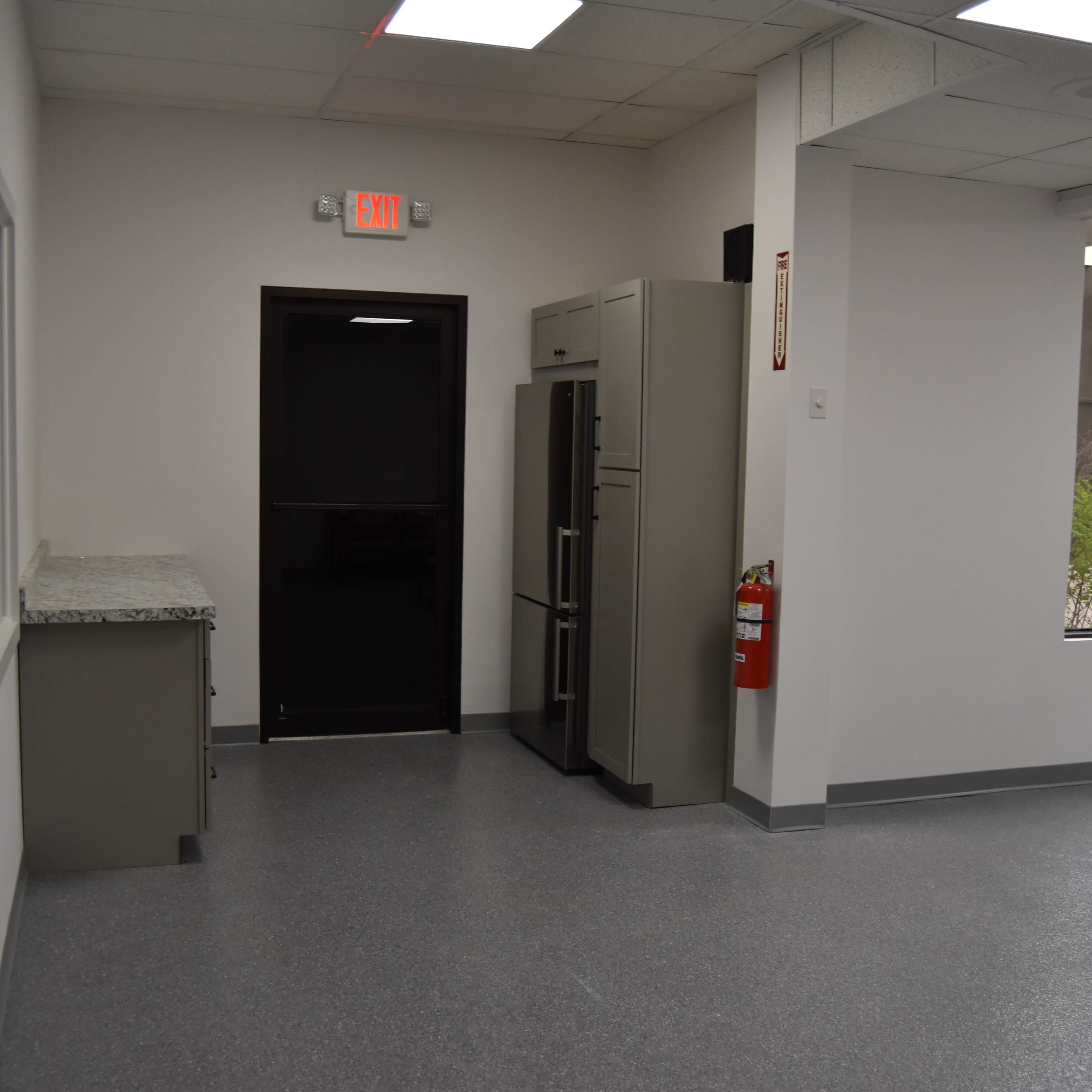 A kitchen area with a countertop, a refrigerator, a black door, and a fire extinguisher mounted on the wall.
