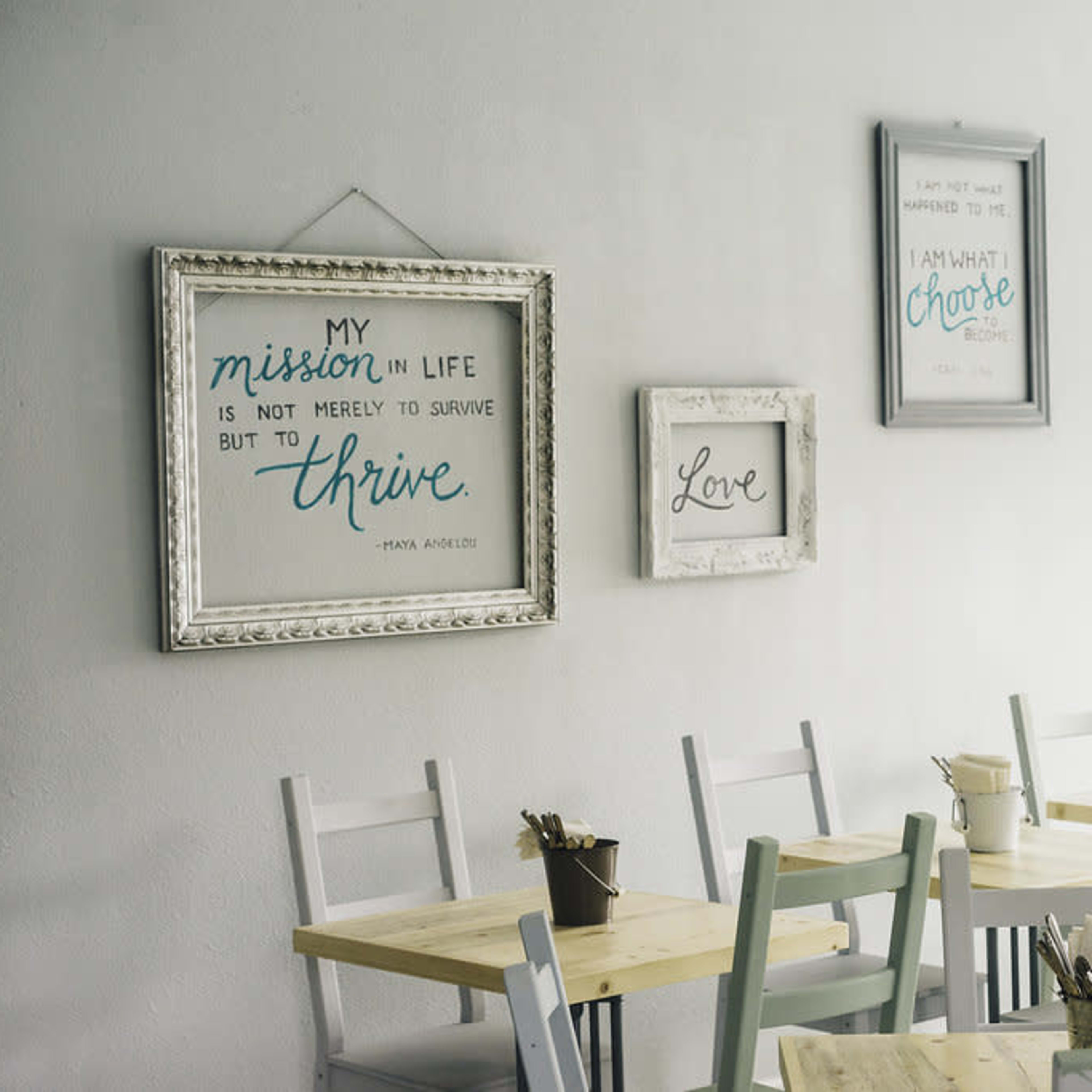 A minimalist café interior with framed inspirational quotes on the walls and wooden tables and chairs arranged neatly.