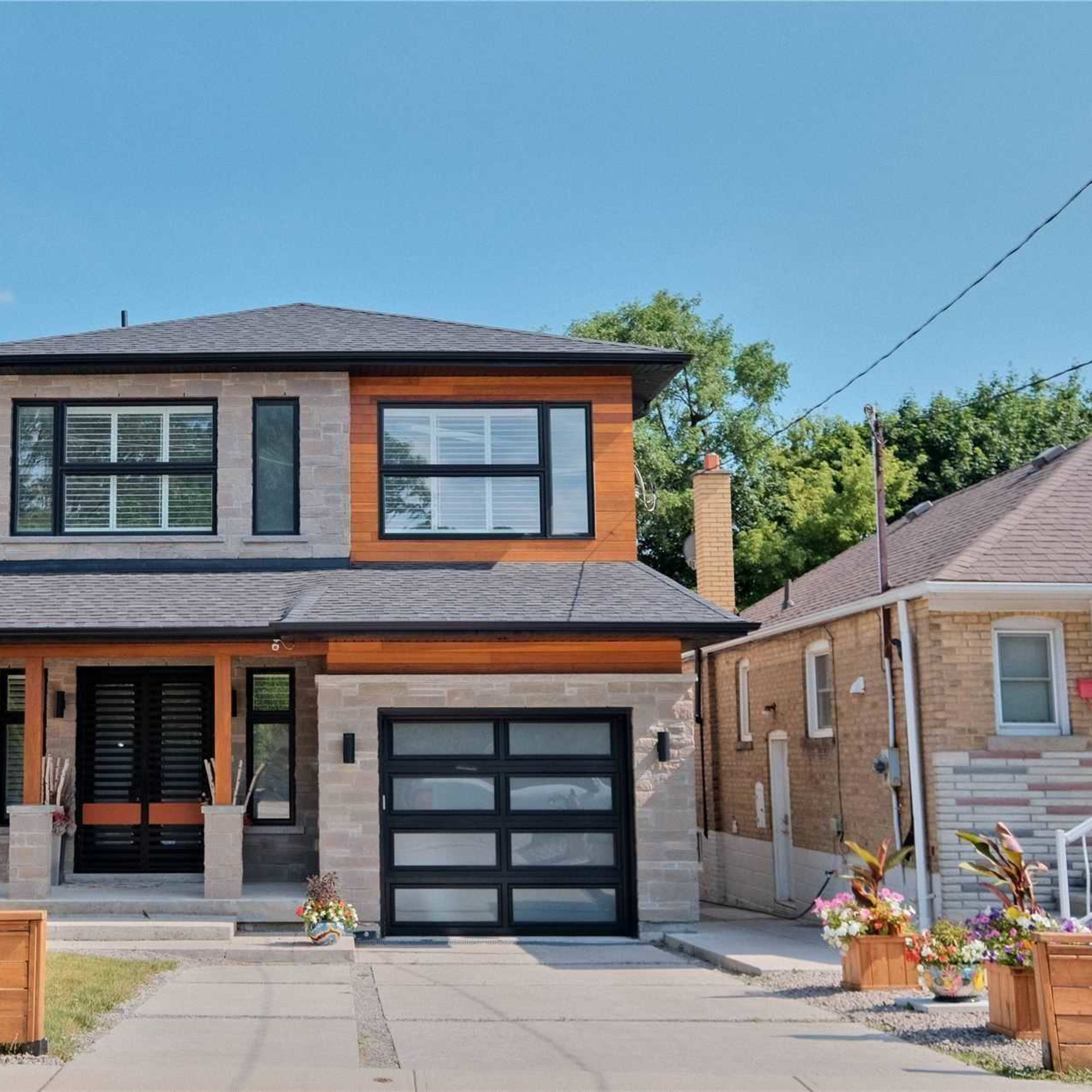A modern two-story house with a mix of stone and wood siding, a black garage door, and landscaped front yard.