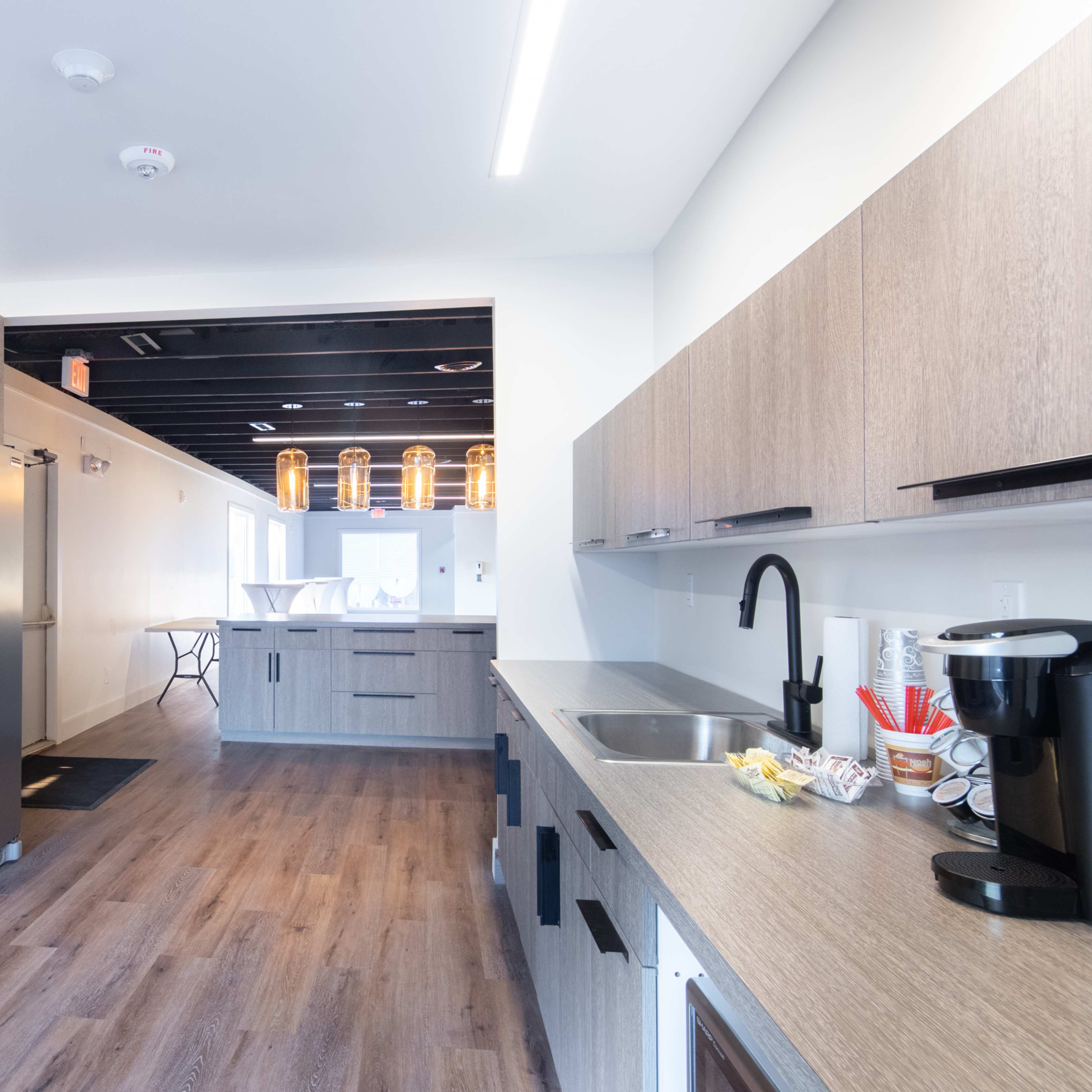 A modern kitchen with grey cabinetry, stainless steel appliances, and a light wood floor, featuring an open layout leading to another room.