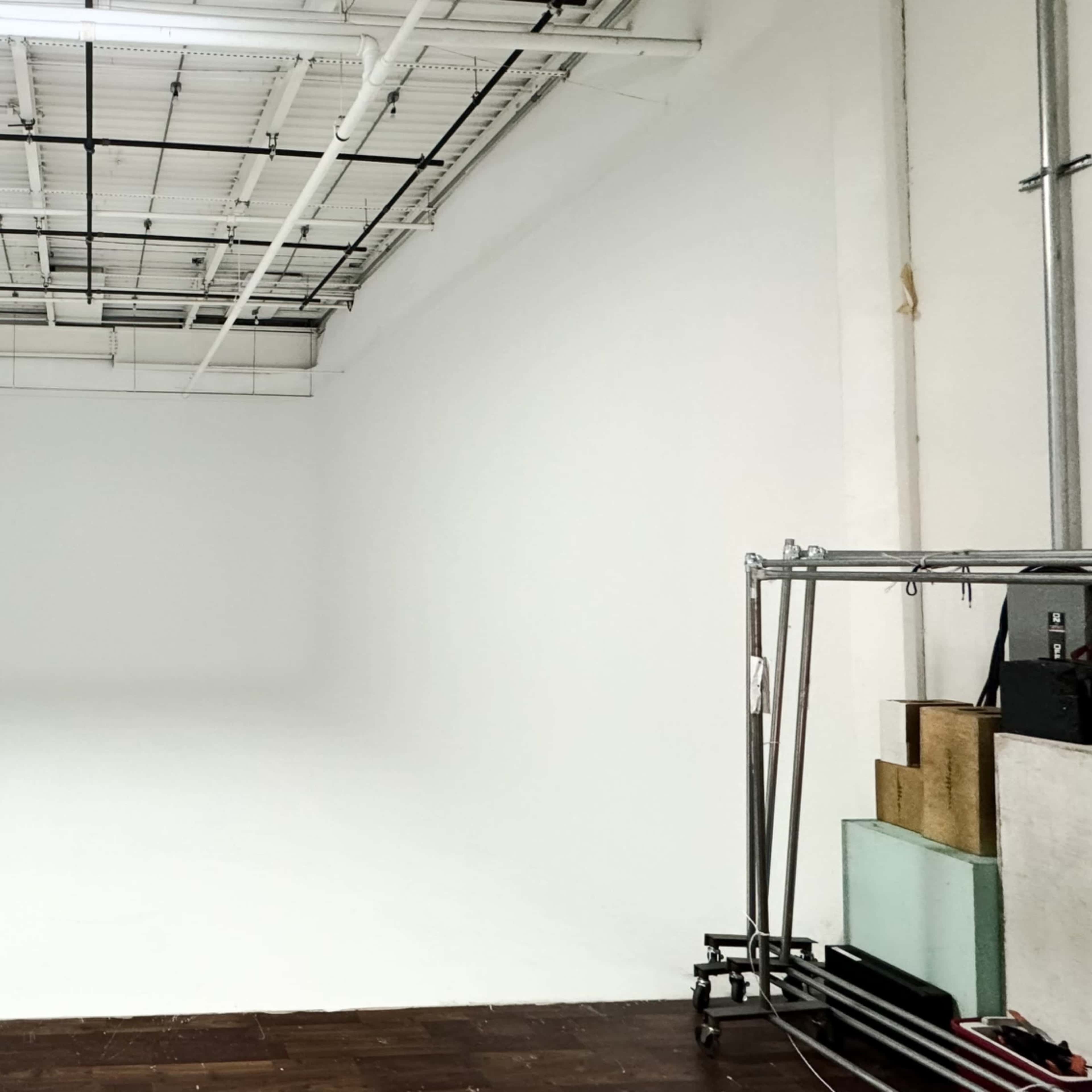 A large, empty studio space with white walls and a clean floor, featuring some equipment on the right side.
