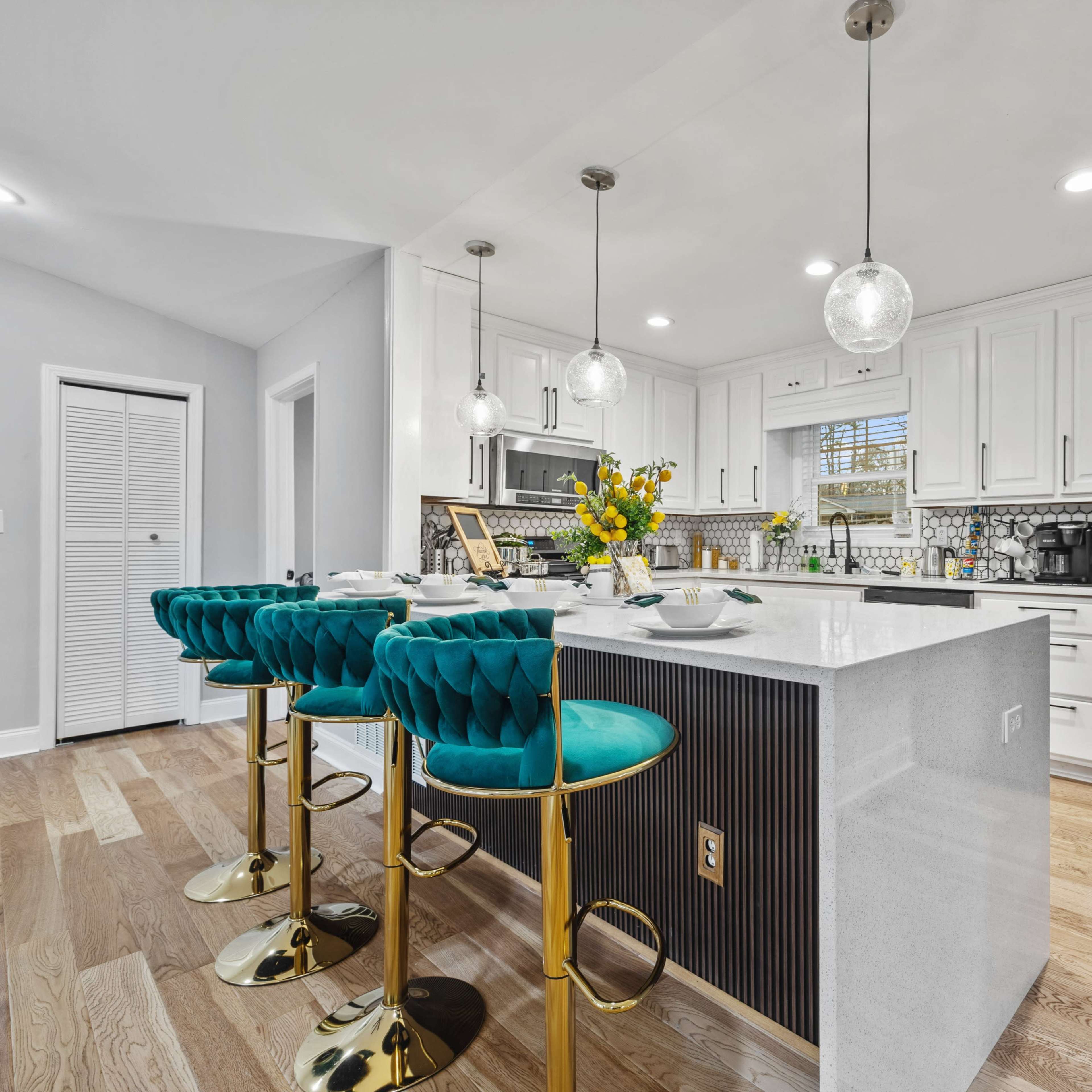A modern kitchen featuring a large island with teal bar stools, stainless steel appliances, and white cabinetry.