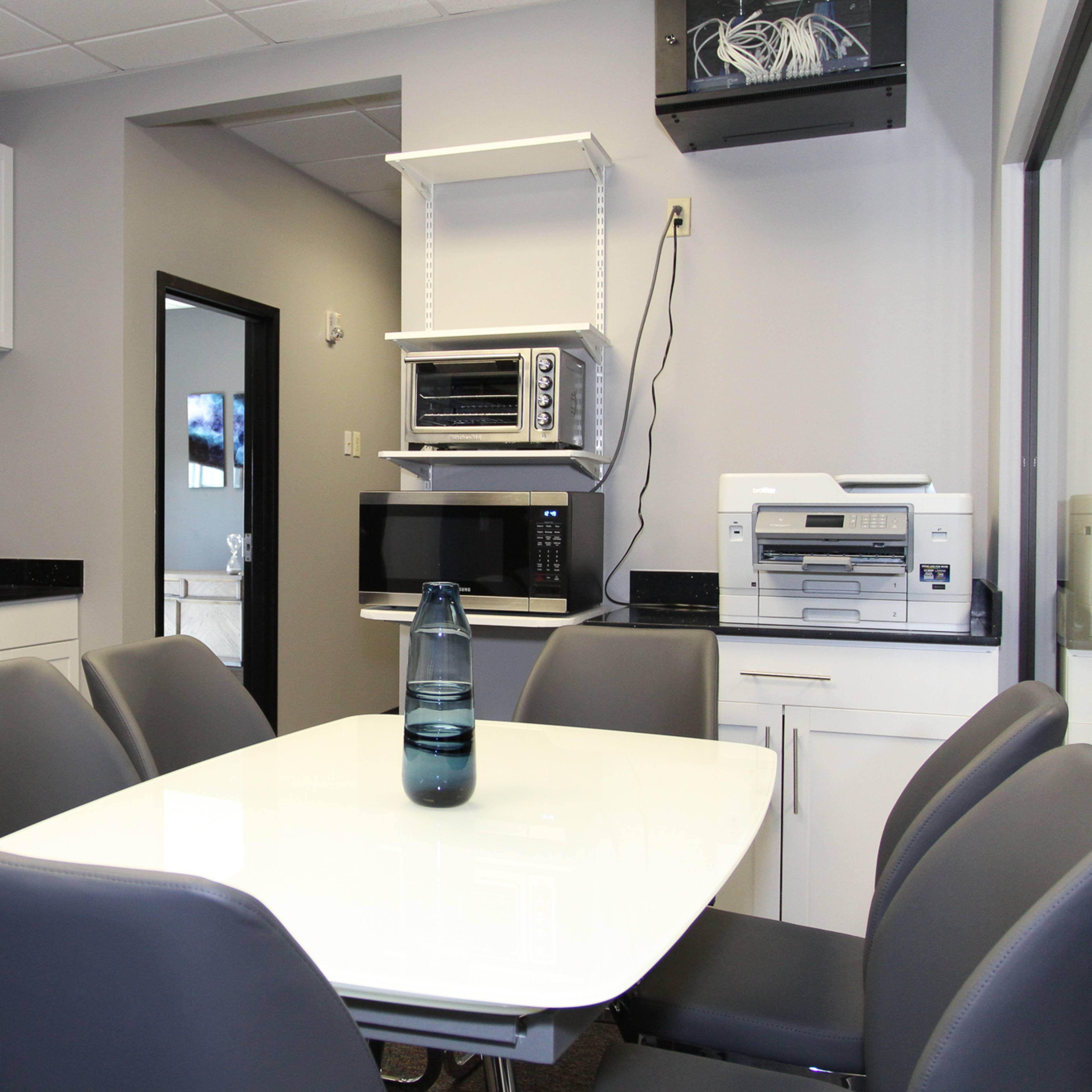 A modern kitchen features stainless steel appliances, a white table with six chairs, and a simple countertop setup with a water bottle.