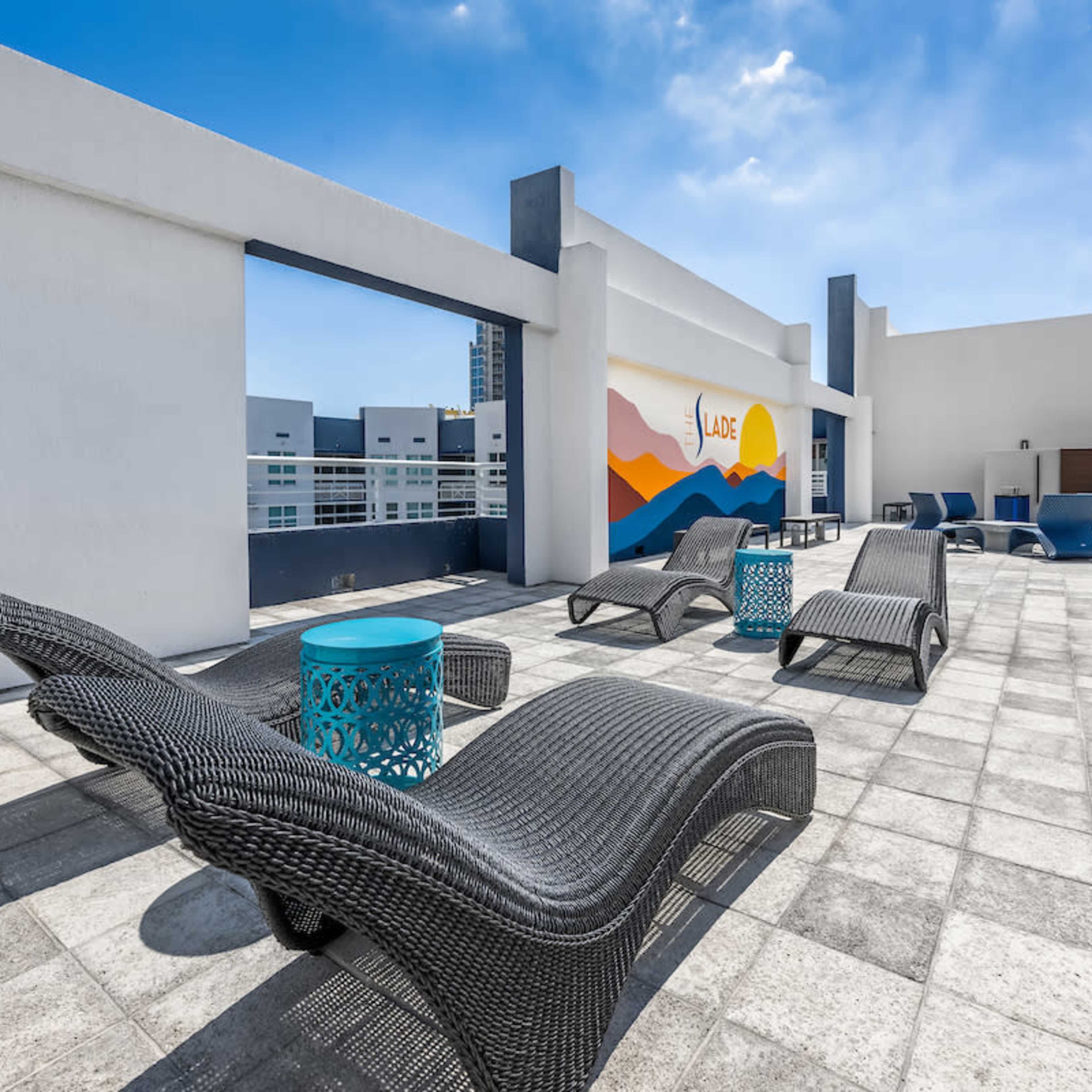 A rooftop terrace features several lounge chairs and tables under a clear blue sky.