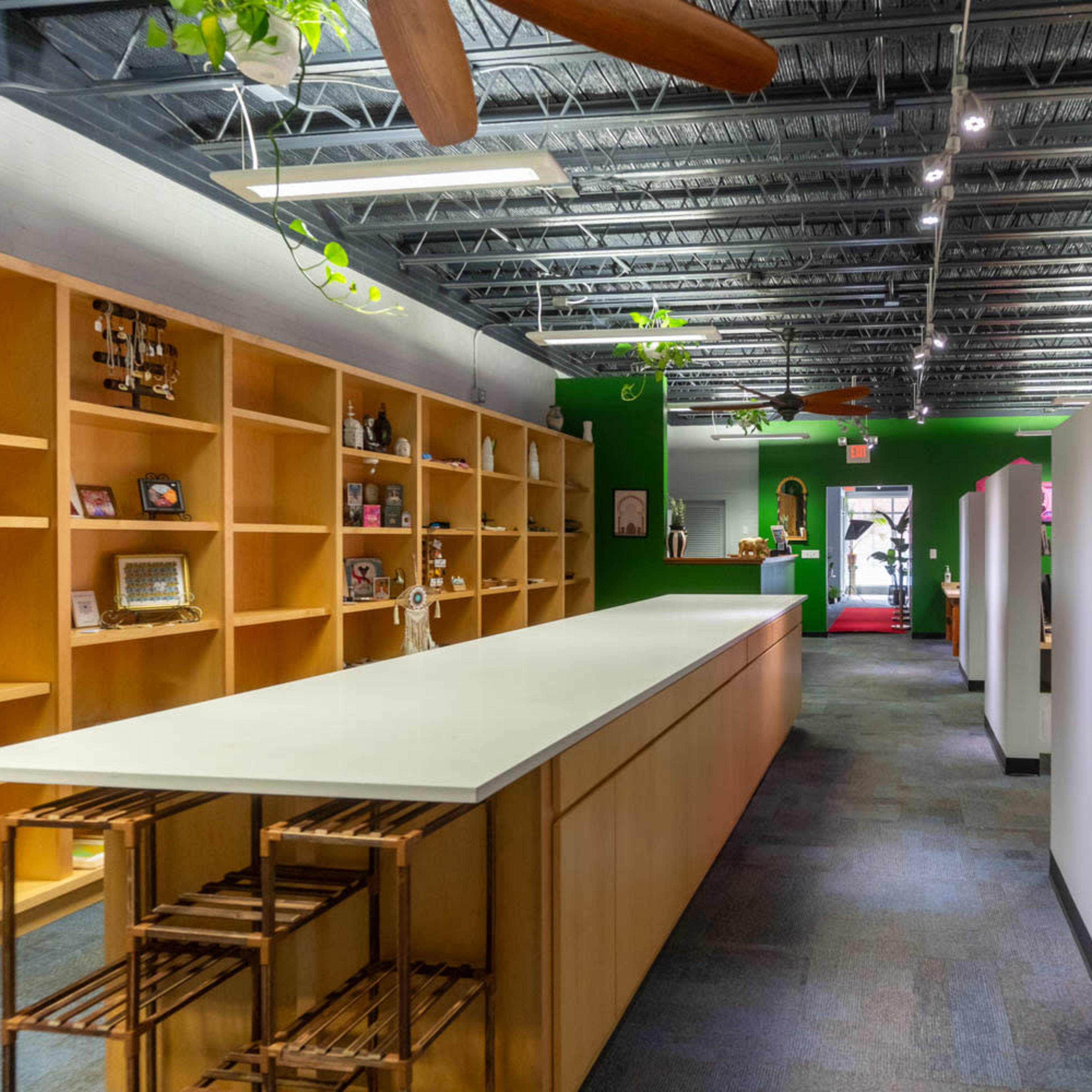 A modern office space with wooden shelves on one side, a long countertop in the center, and bright green walls accented by potted plants.