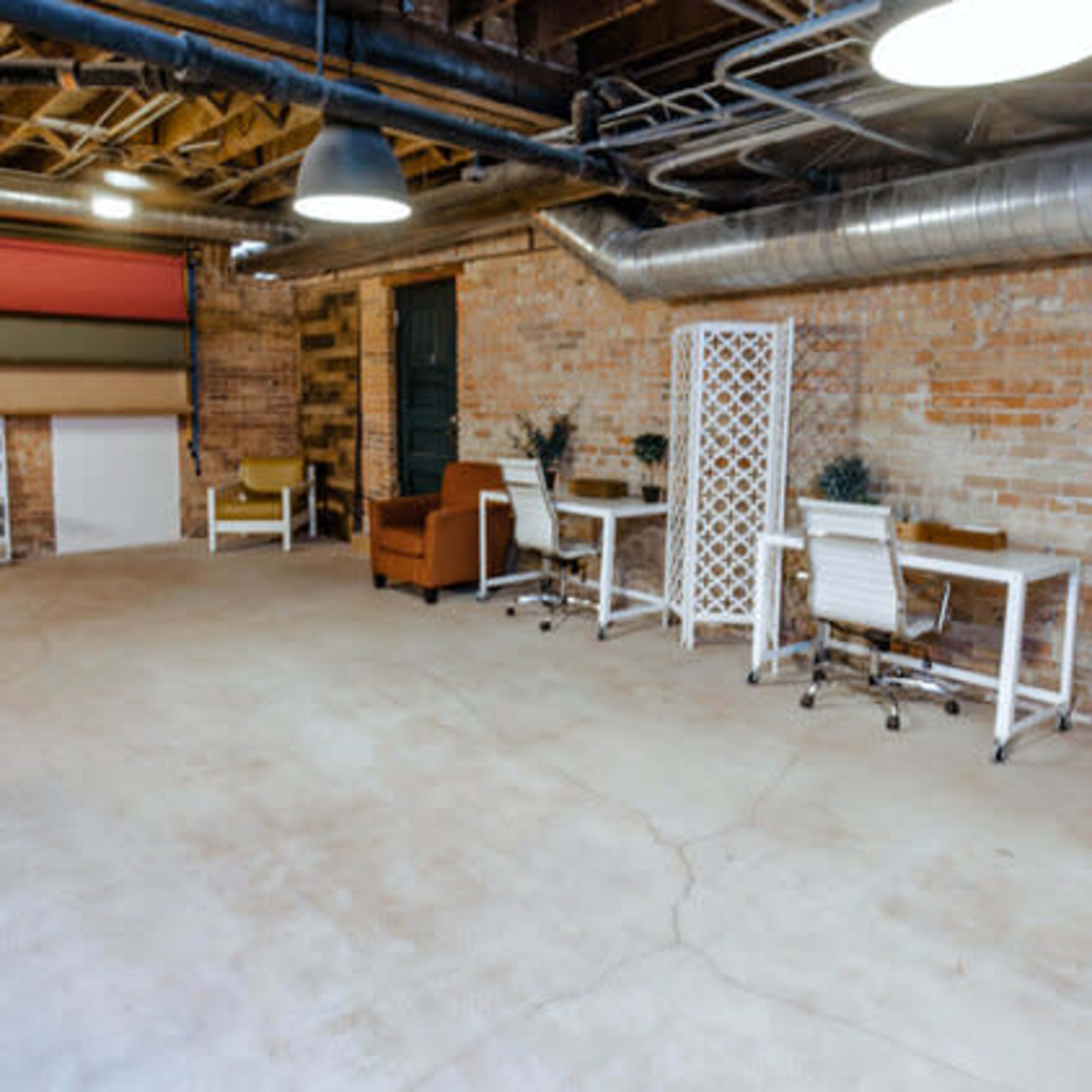 A spacious, industrial-style basement office with exposed brick walls, a concrete floor, and various seating arrangements and workstations.