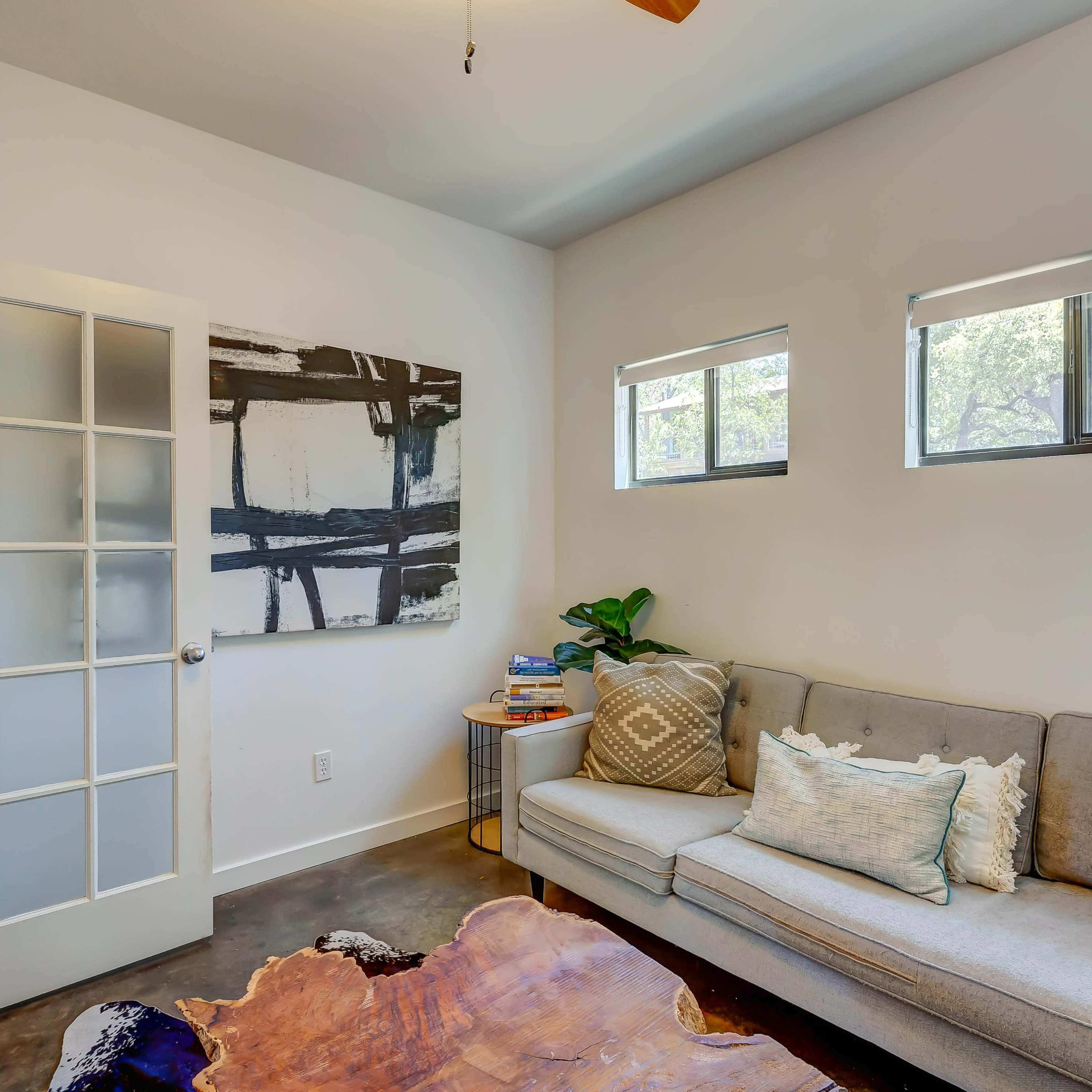 A modern living room features a gray sofa with decorative pillows, a wooden coffee table, and a glass door leading to another space.