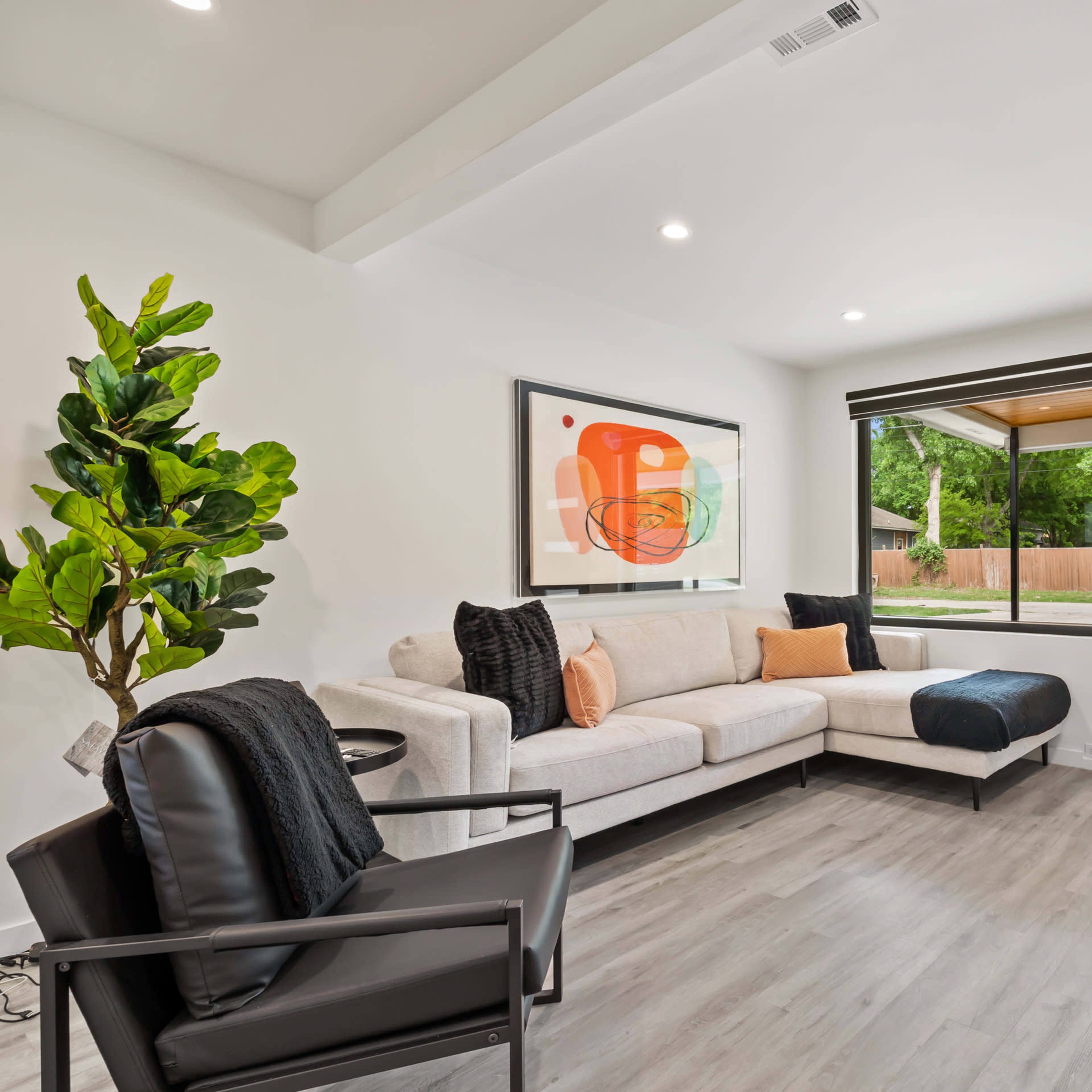 The modern living room features a light-colored sofa, a black armchair, a large window, and a digital fireplace wall.