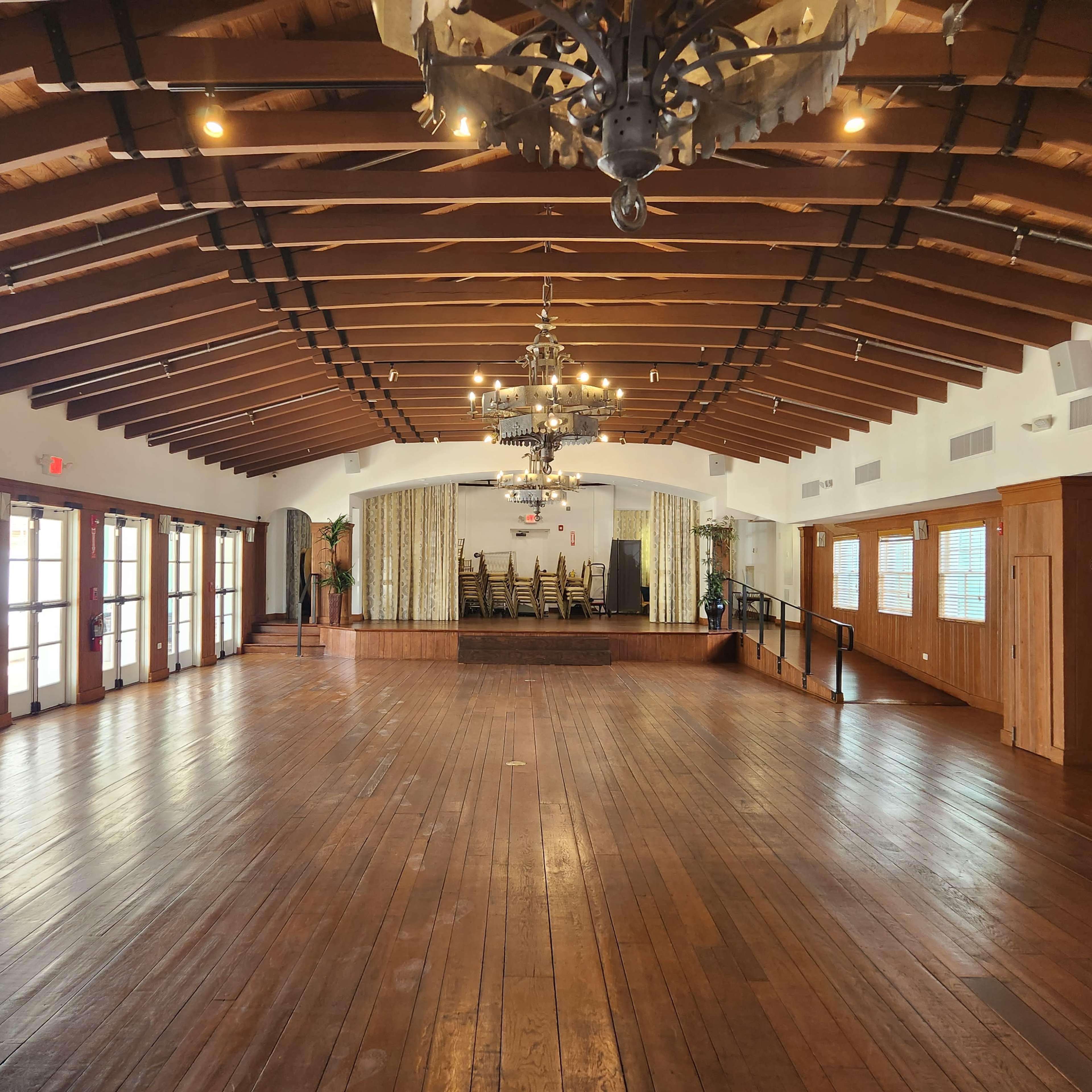 A spacious interior room with wooden floors, exposed beams, and a stage area at one end.