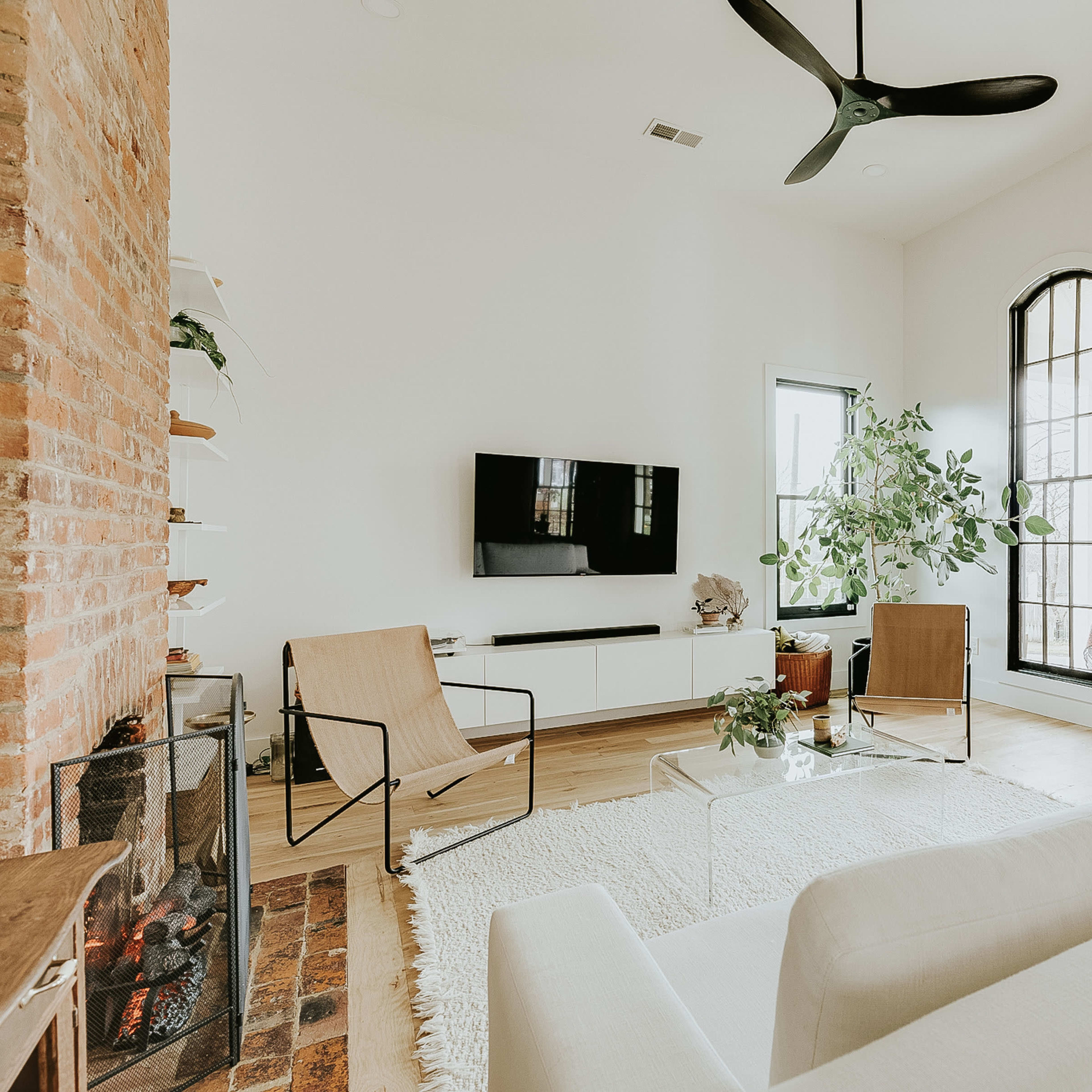 The living room features a white sofa, two chairs, a glass coffee table, and a large window with a view of greenery.