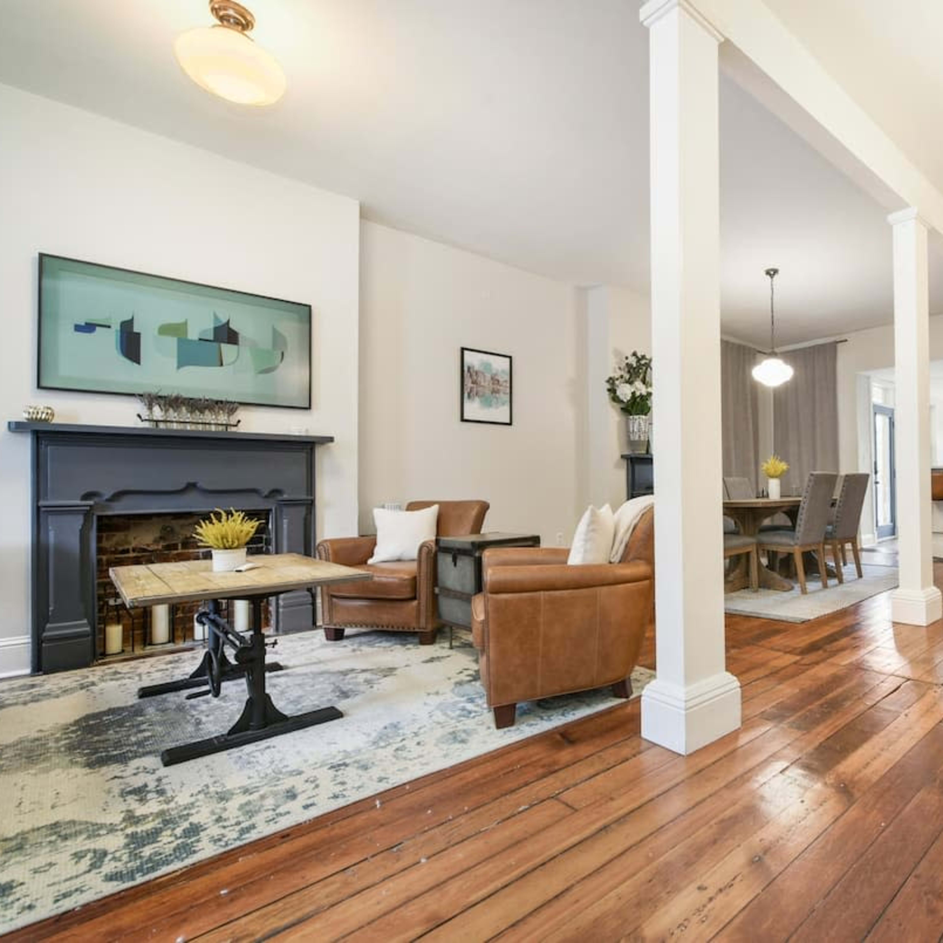 A bright, open interior space with a living area featuring leather chairs, a wooden table, and a staircase leading to an upper level.