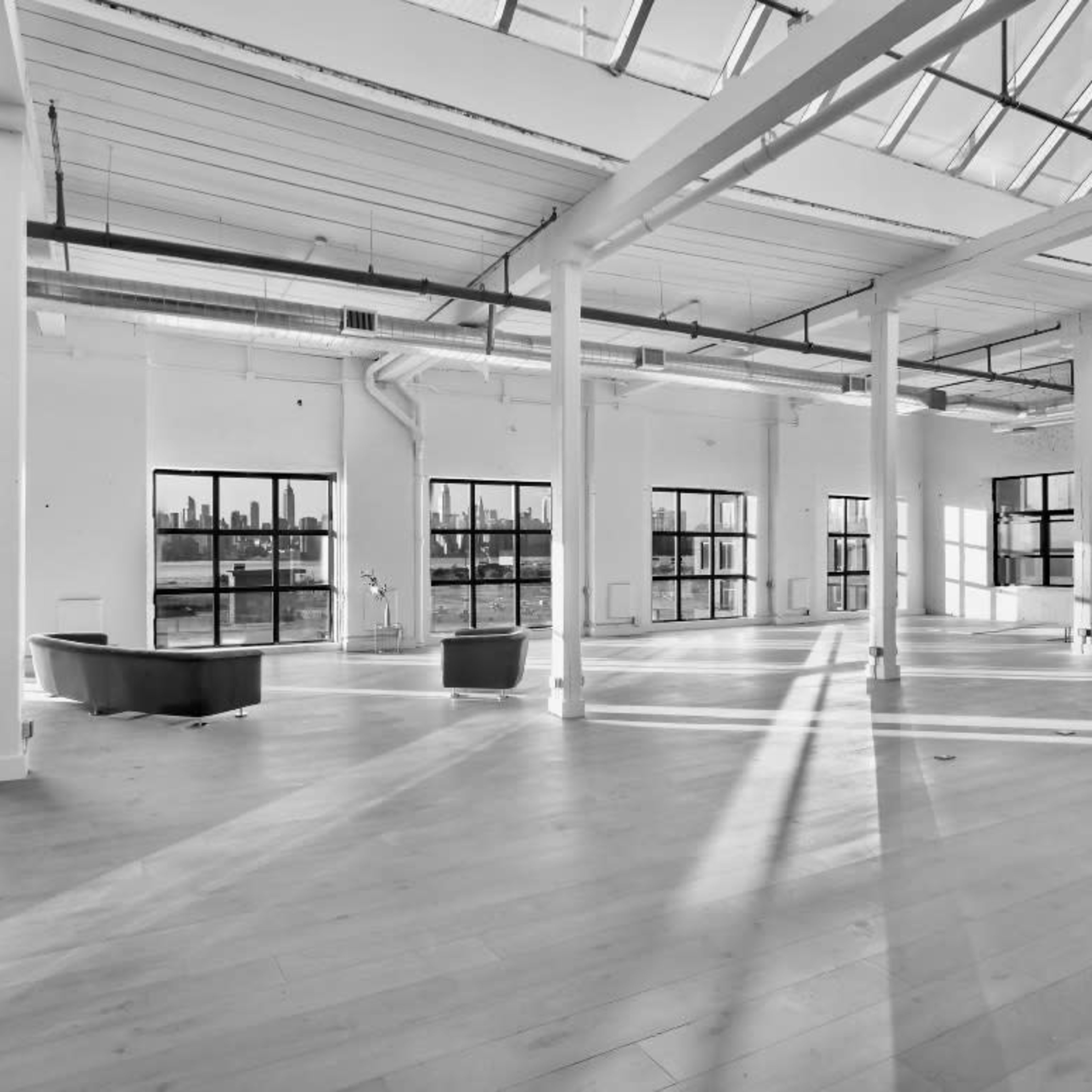 A spacious, empty industrial-style room with large windows that provide a view of a city skyline.