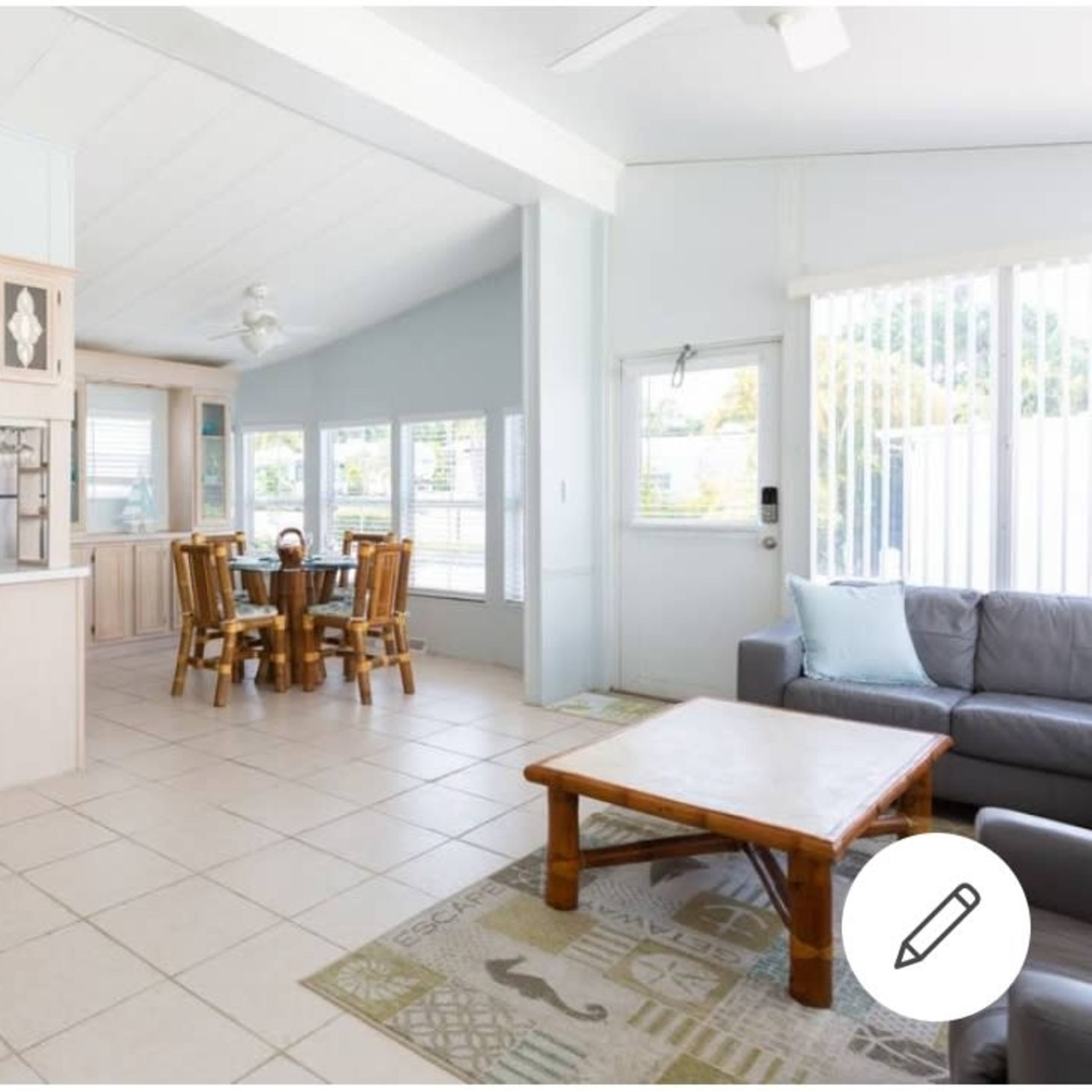 An open-concept living area featuring a kitchen with wooden cabinetry, a dining table with four chairs, and a seating area with a gray sofa.
