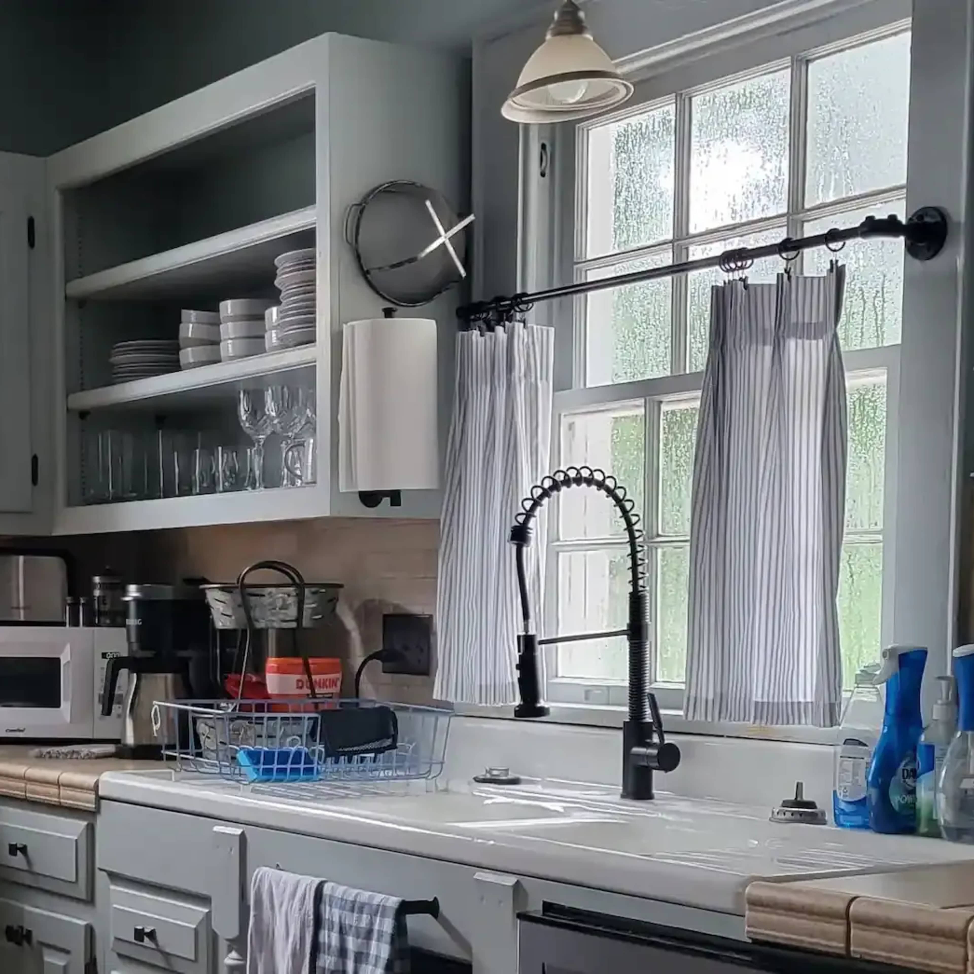 A kitchen with light gray cabinets, a white sink, and a window above it, displaying dishes and kitchen appliances.