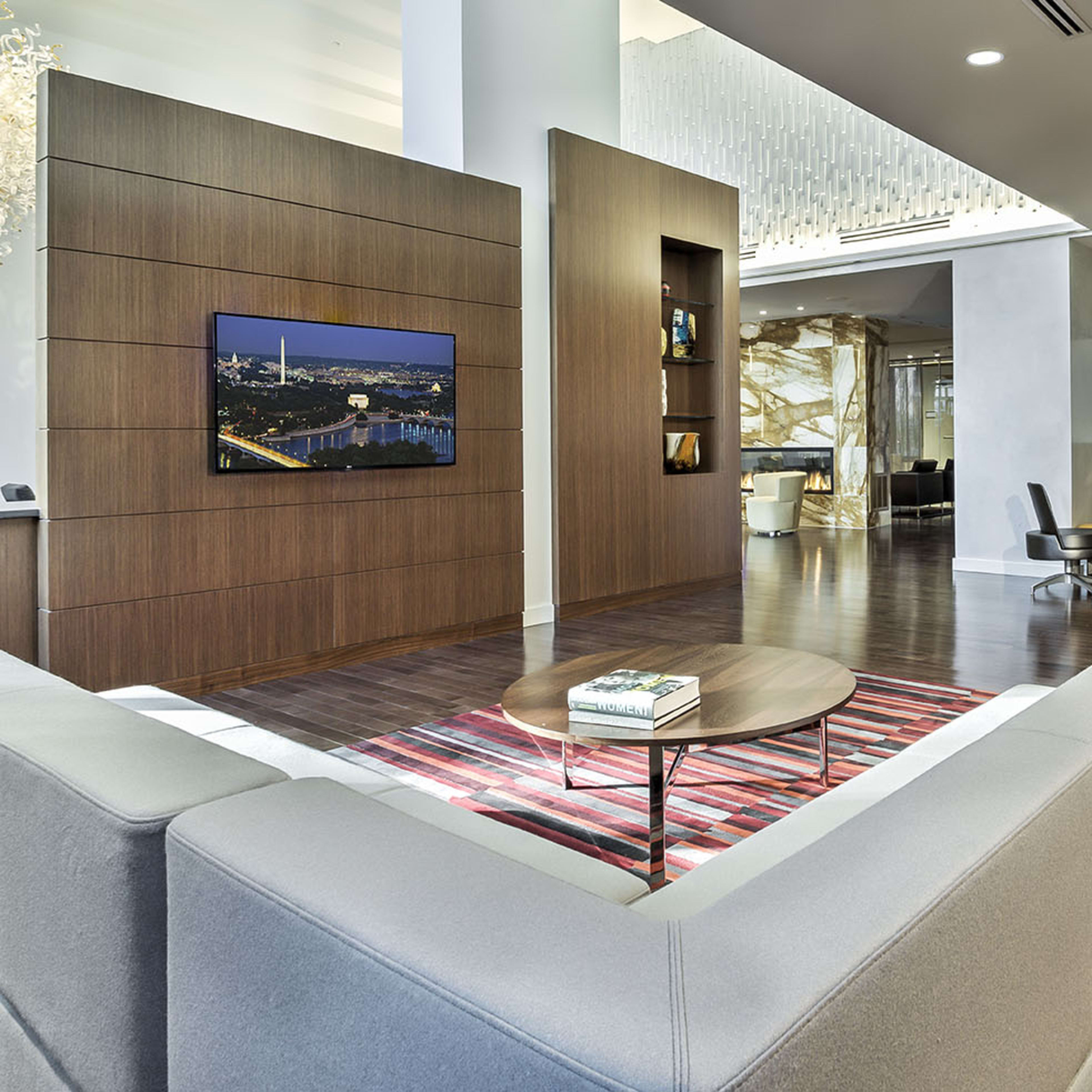 A modern lounge area featuring a gray sofa, a wooden wall-mounted television, and stylish seating arrangements on a hardwood floor.